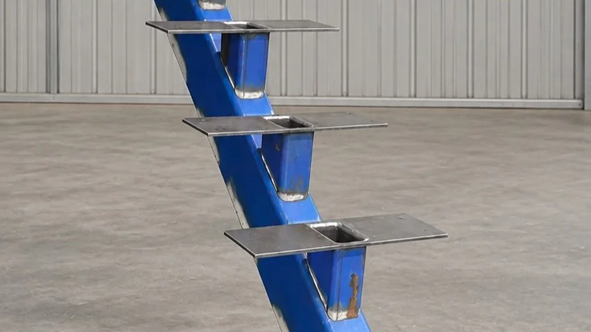 A metal staircase with three steps, painted blue with visible rust, situated indoors against a corrugated metal wall.