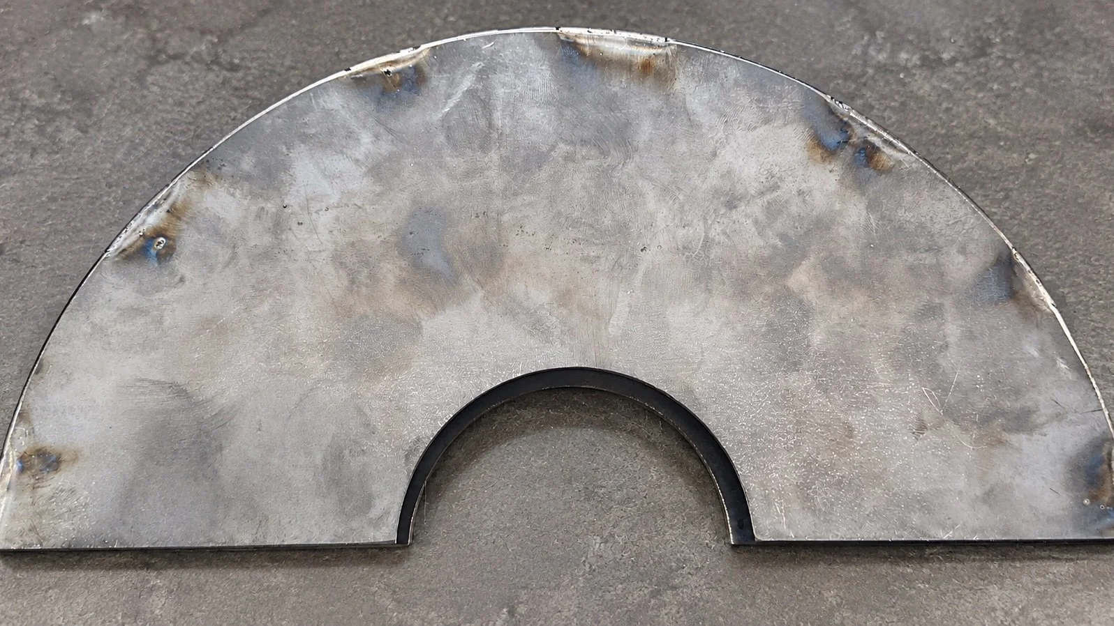 Metal semi-circular object with a cutout in the middle, resting on a rough gray surface.