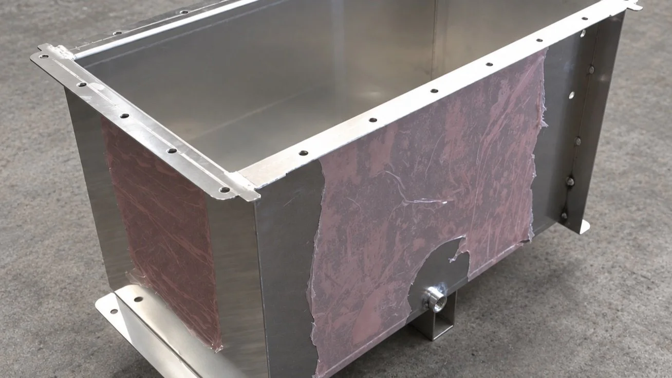 A rectangular metal enclosure with a shiny interior and partially covered exterior sides, placed on a flat surface.