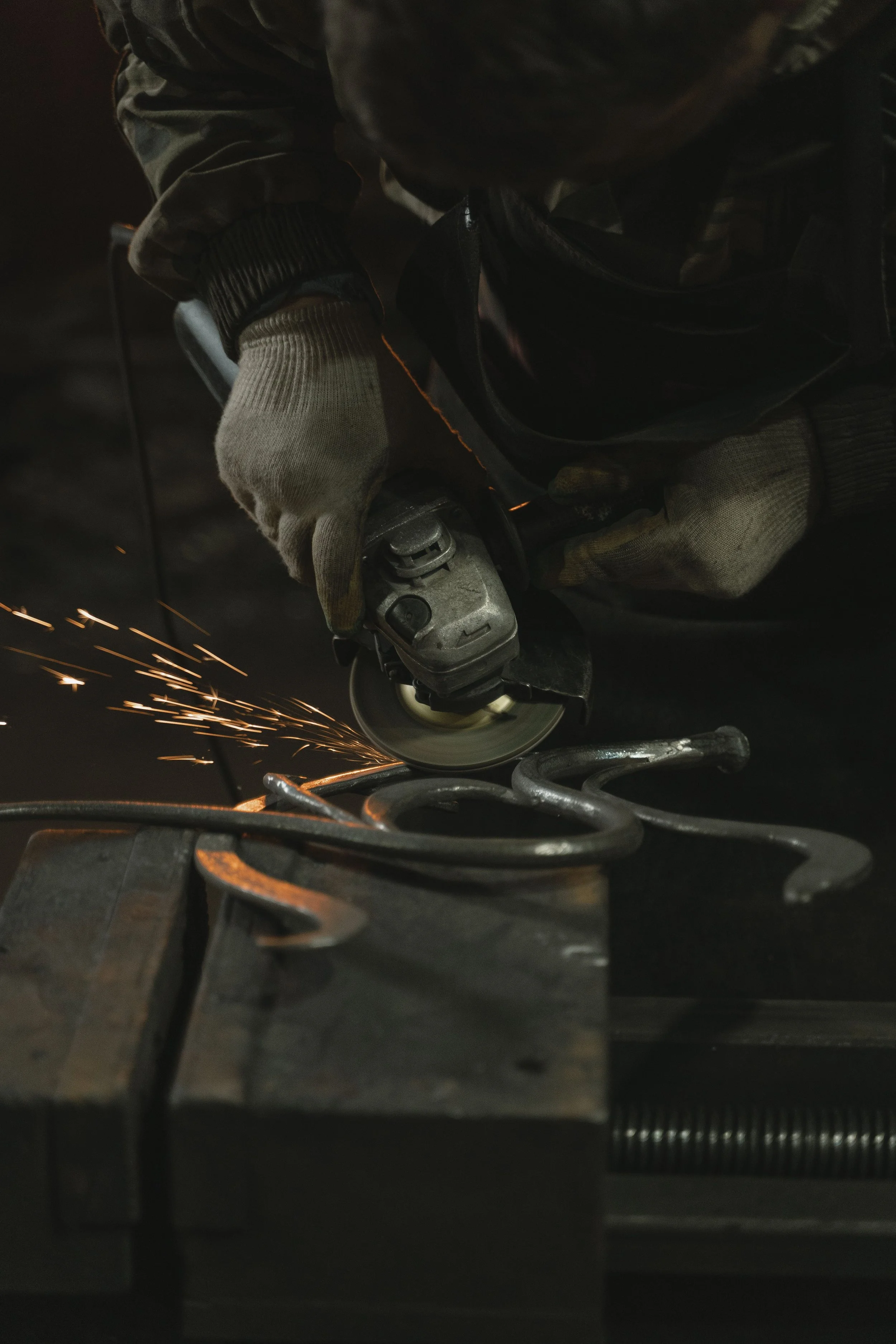 Person wearing gloves using an angle grinder to cut metal, sparks flying in a dark environment.