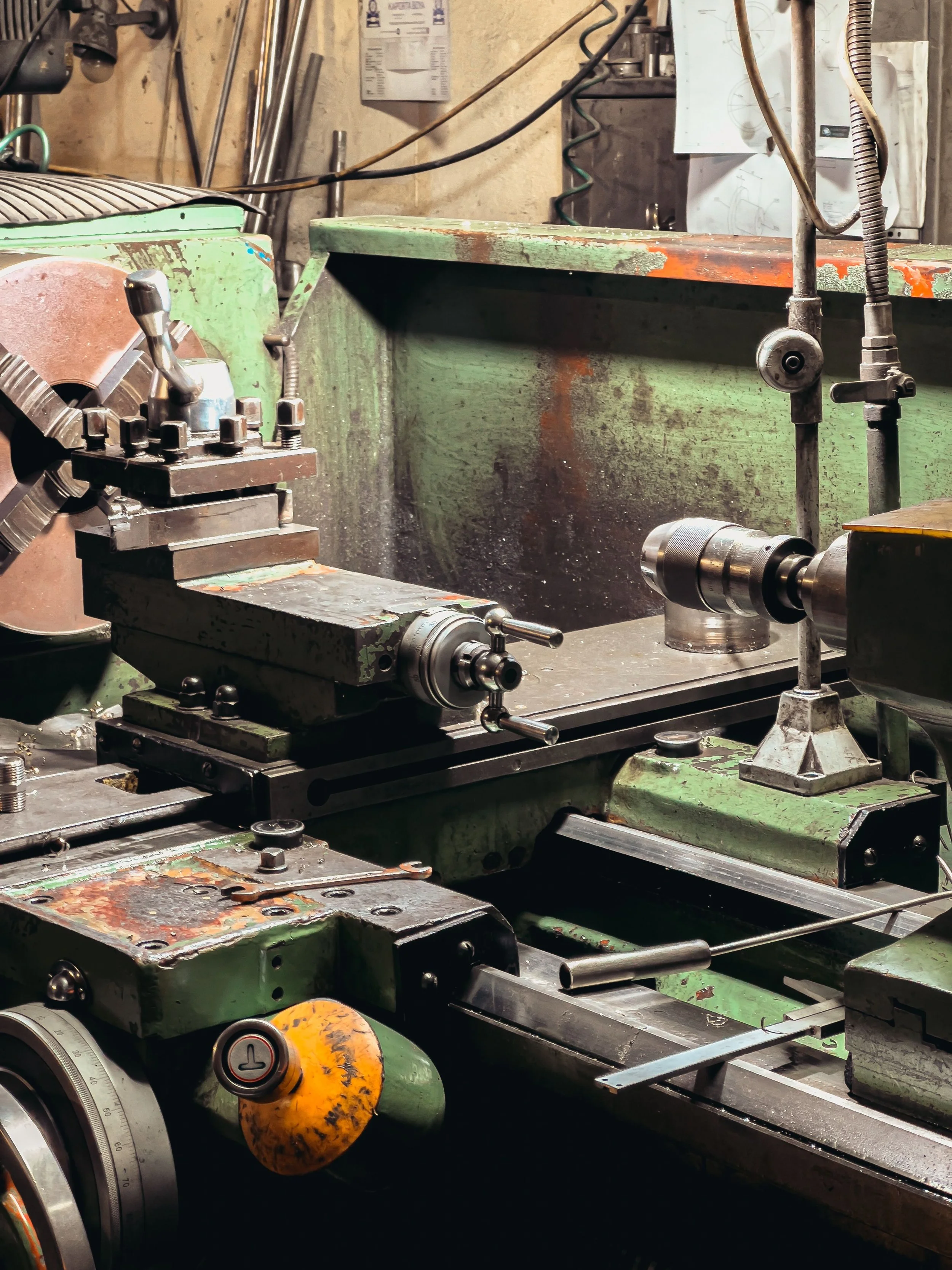 Close-up of a green metal lathe machine with various tools and components in a workshop setting.