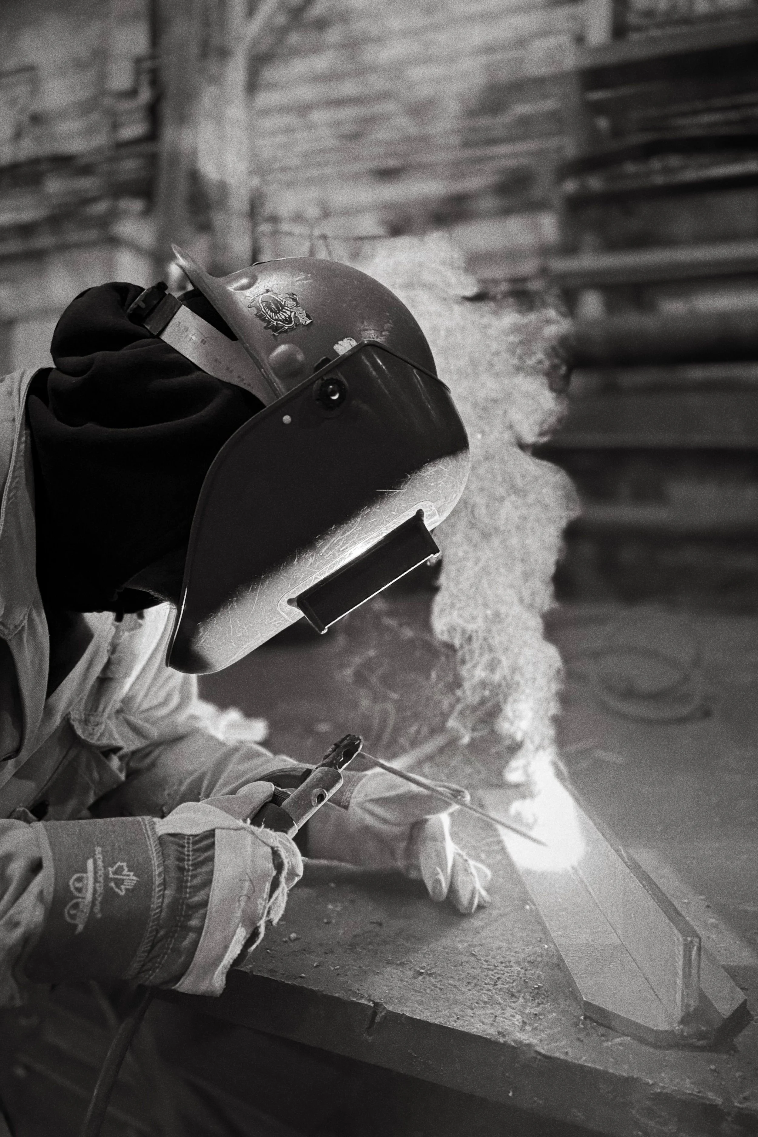 A worker in protective gear welding metal on a work surface, with sparks flying, in an industrial setting.