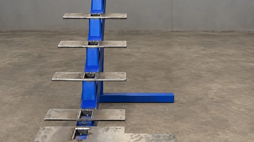 A blue mobile workbench with six metal shelves, positioned on a concrete floor in front of a plain wall.