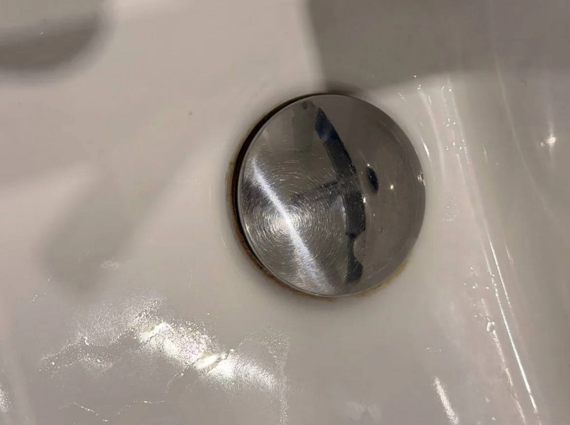Close-up of a metallic drain in a white sink.