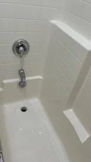 Close-up of a shower or bathtub faucet with a shower head above and a white tiled wall in the background.