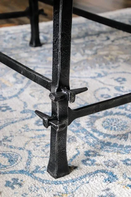 Close-up of the leg and support brace of a black metal table on a patterned rug.