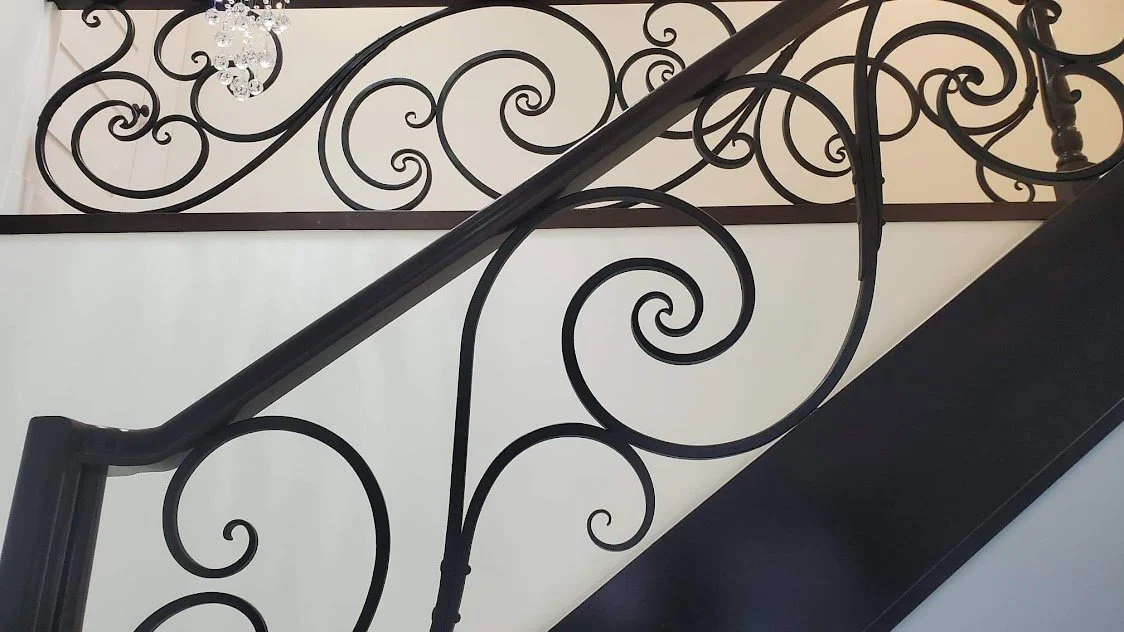 Close-up of a decorative black wrought iron staircase railing with swirling patterns.