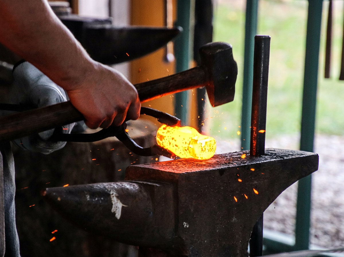 Blacksmith forging hot metal with hammer and tongs in a blacksmith shop.