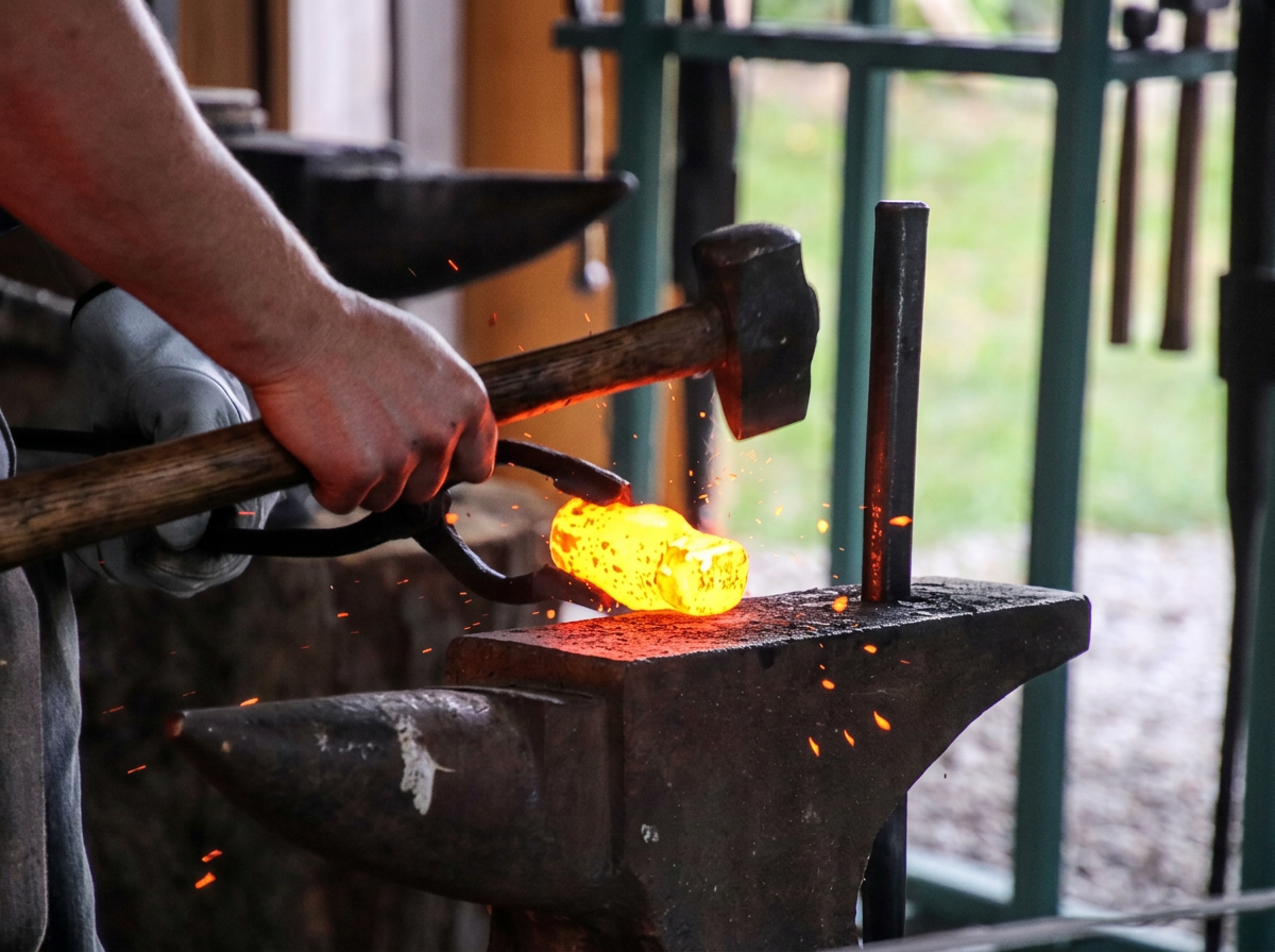 A person blacksmithing with a hammer on a glowing piece of heated metal on an anvil, sparks flying.