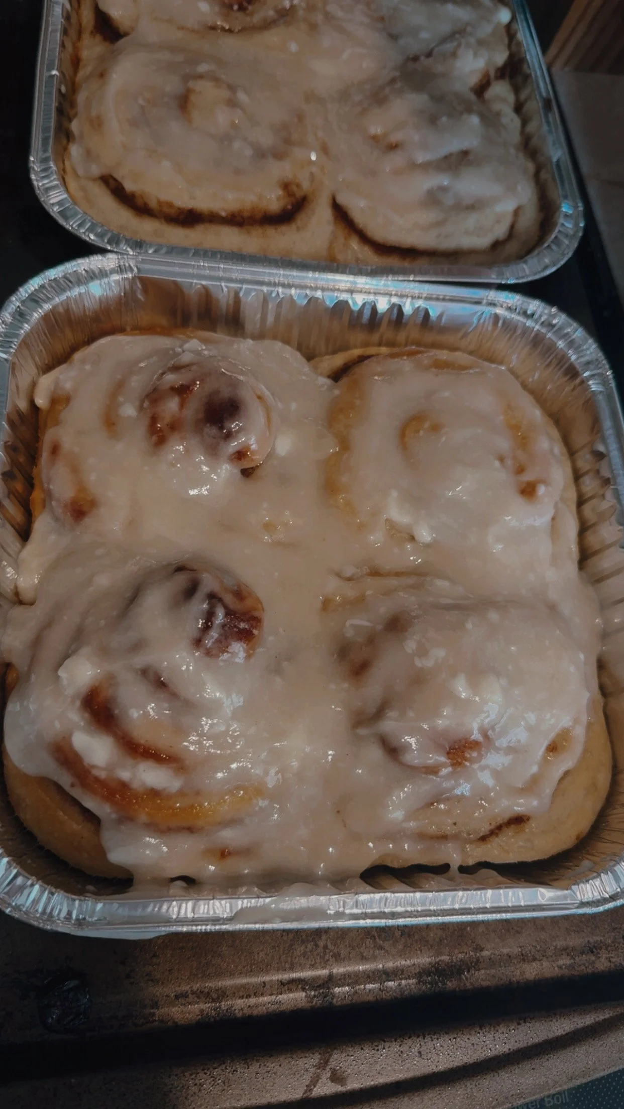 Aluminum containers with cinnamon rolls topped with vanilla icing.