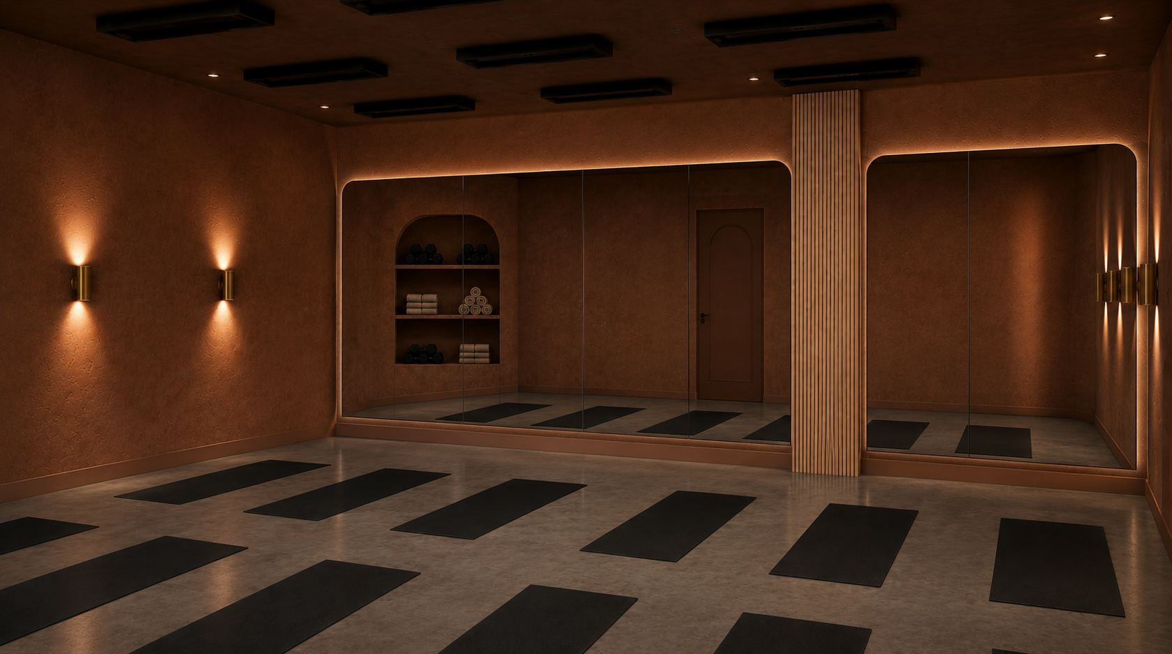 An empty yoga or meditation studio with black mats on the floor, warm lighting, a mirrored wall, and shelves with yoga mats and towels.