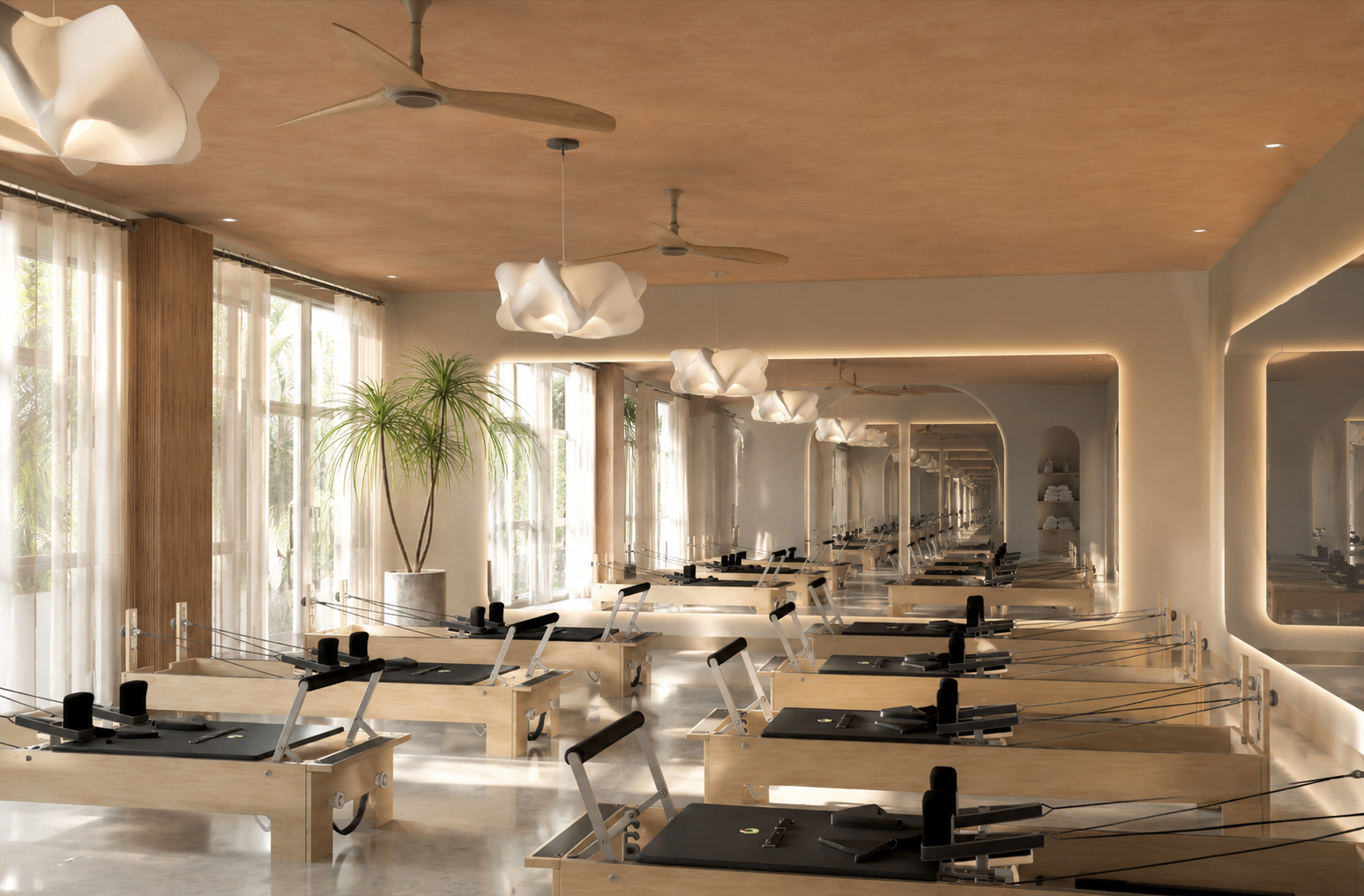 A Pilates studio with multiple reformer machines arranged in rows, large windows with sheer curtains, a potted plant, modern cloud-shaped ceiling lights, and a large mirror reflecting the room's interior.