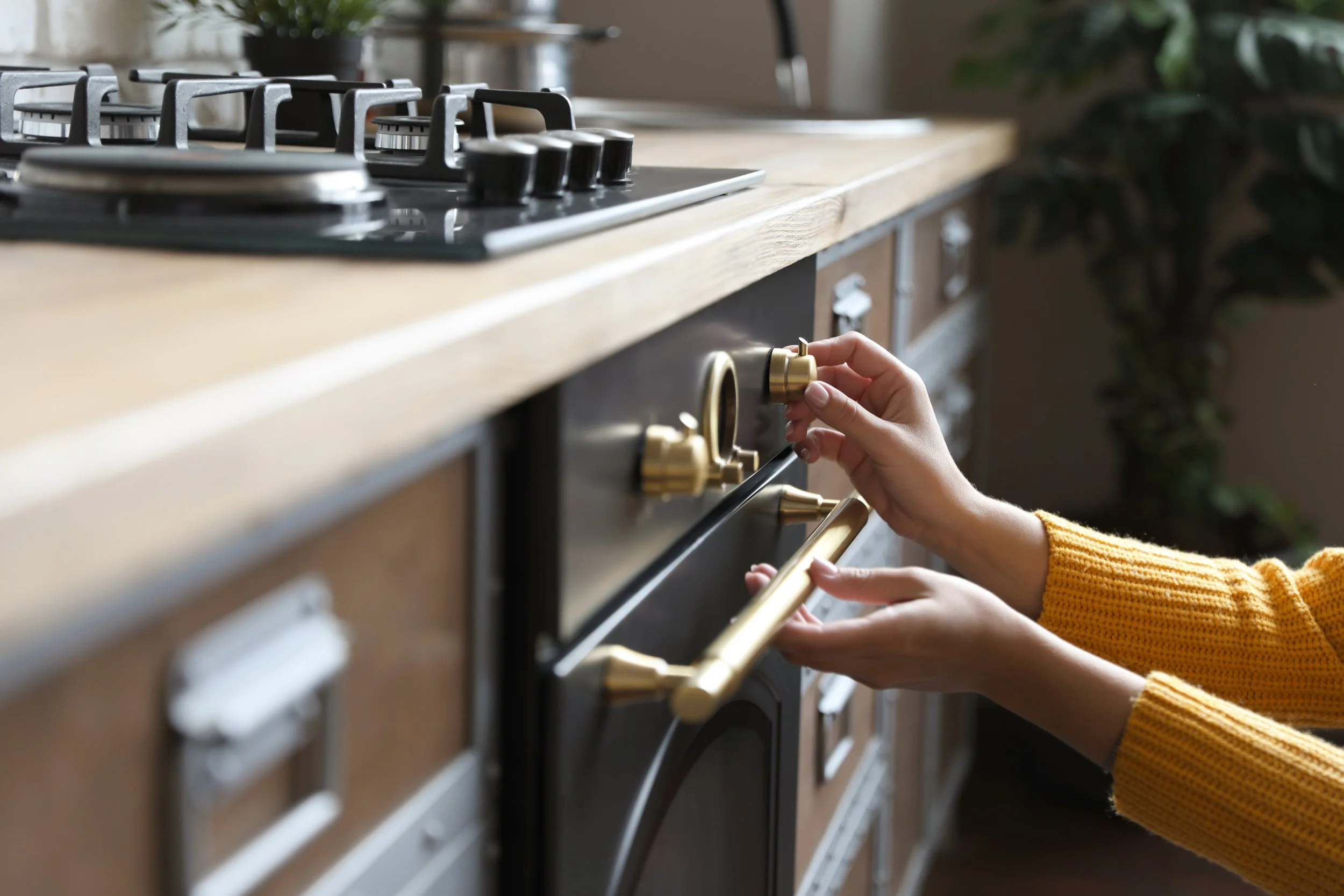 A person in a yellow sweater adjusting the oven temperature knob in a modern kitchen.