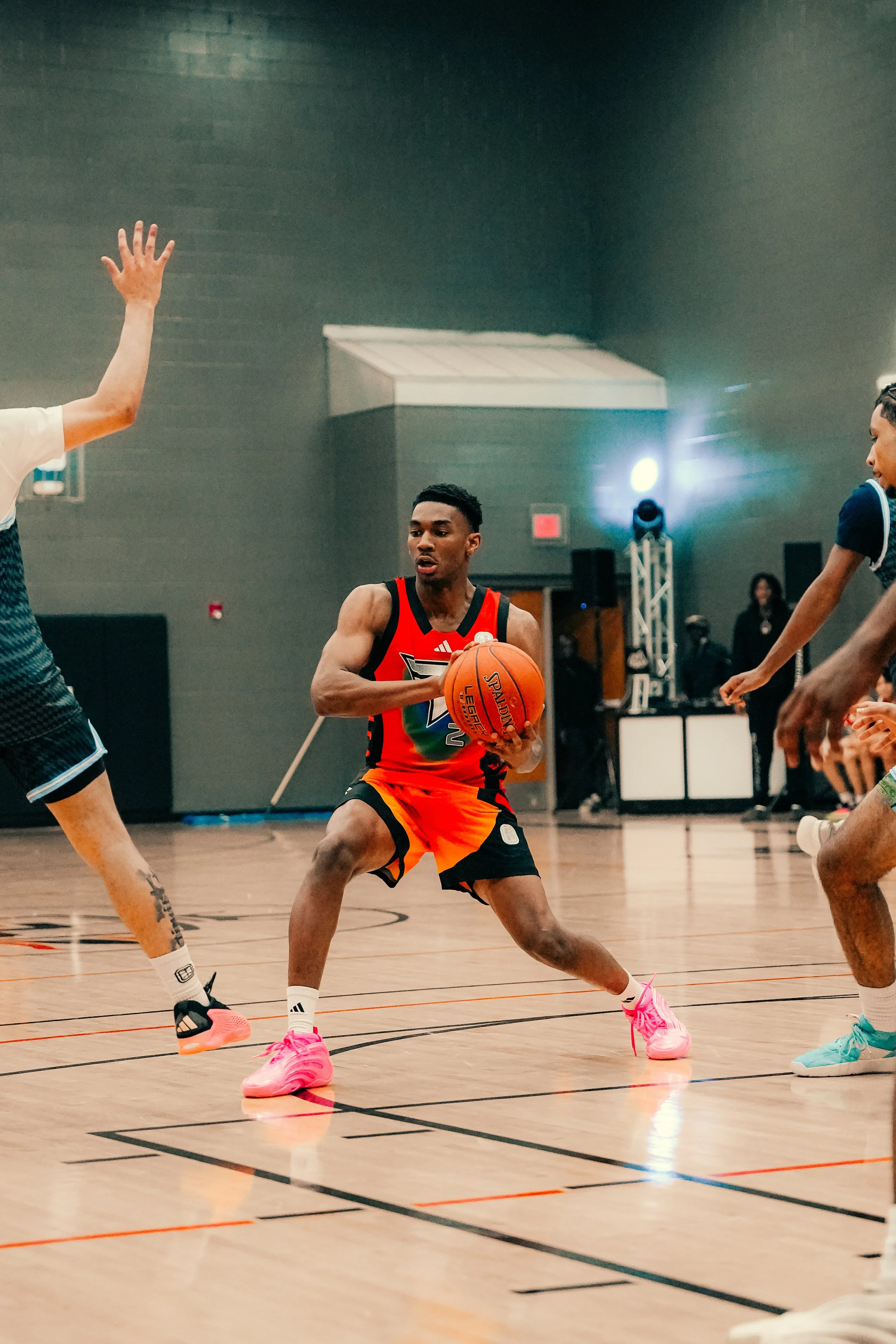 A basketball player in a red and black uniform is dribbling an orange basketball on an indoor court, with other players around him.