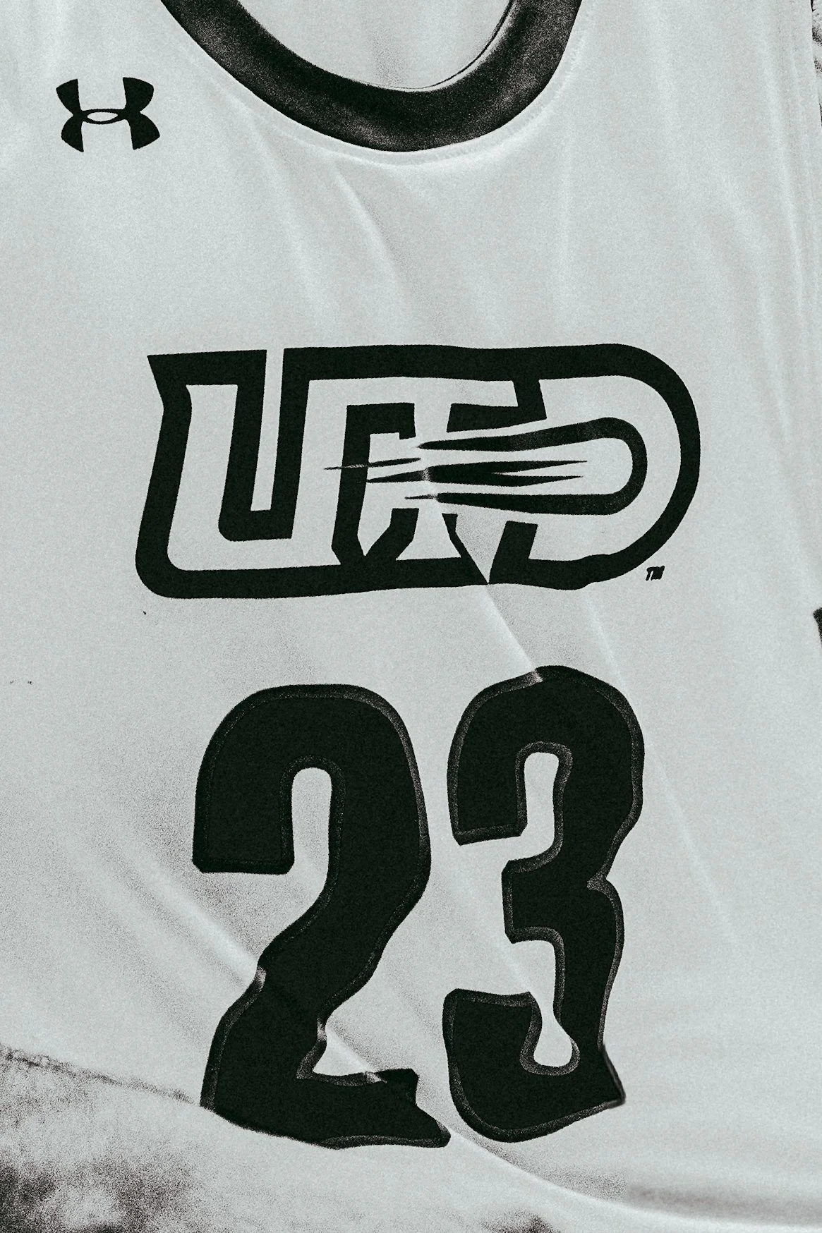 Close-up of a white sports jersey featuring the Under Armour logo, the number 23, and a stylized 'U.S. Army' logo with a mountain outline and flag design.