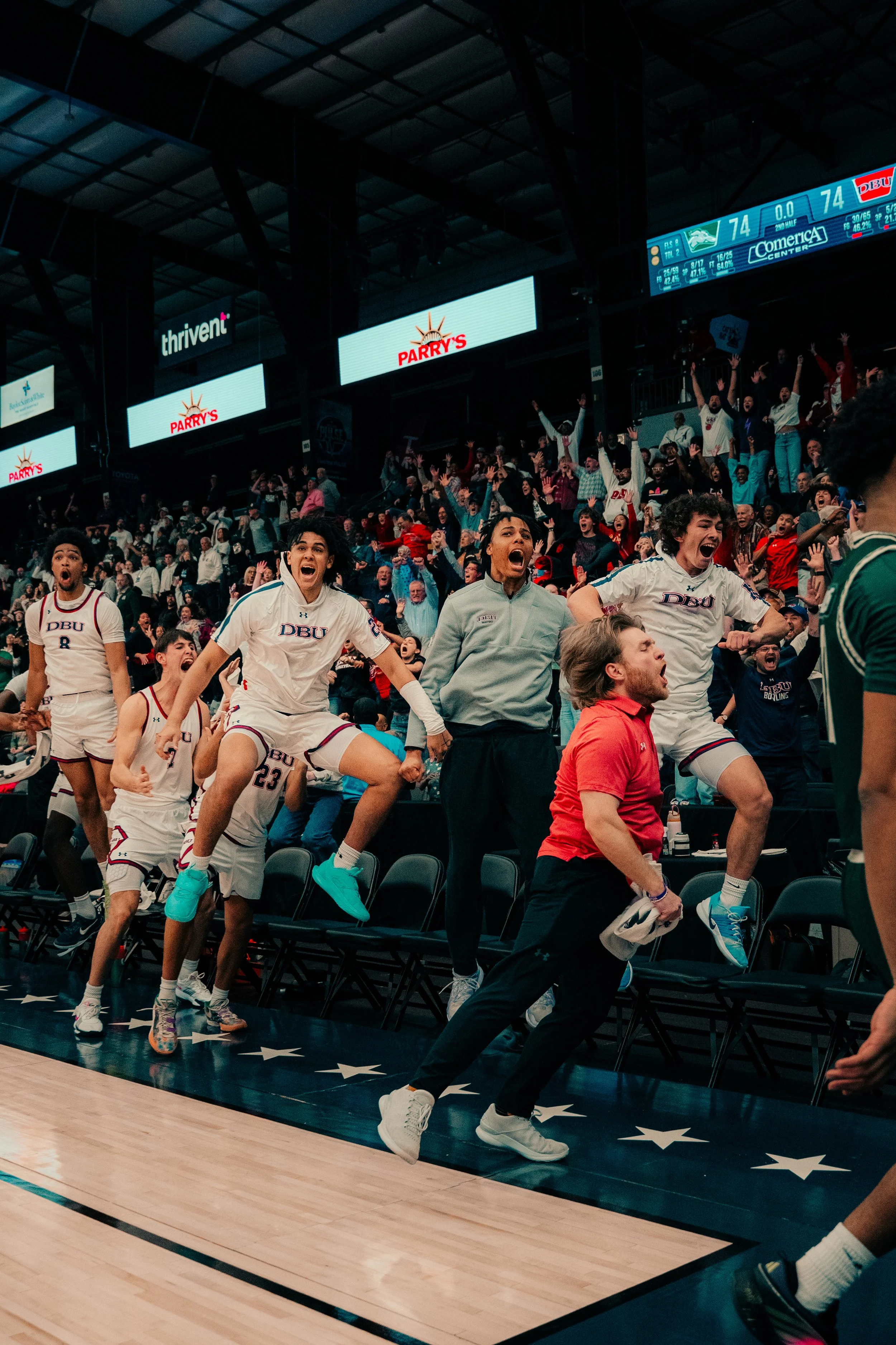 Basketball players and fans celebrating during a game at the arena, with a digital scoreboard showing the score of 74-74.