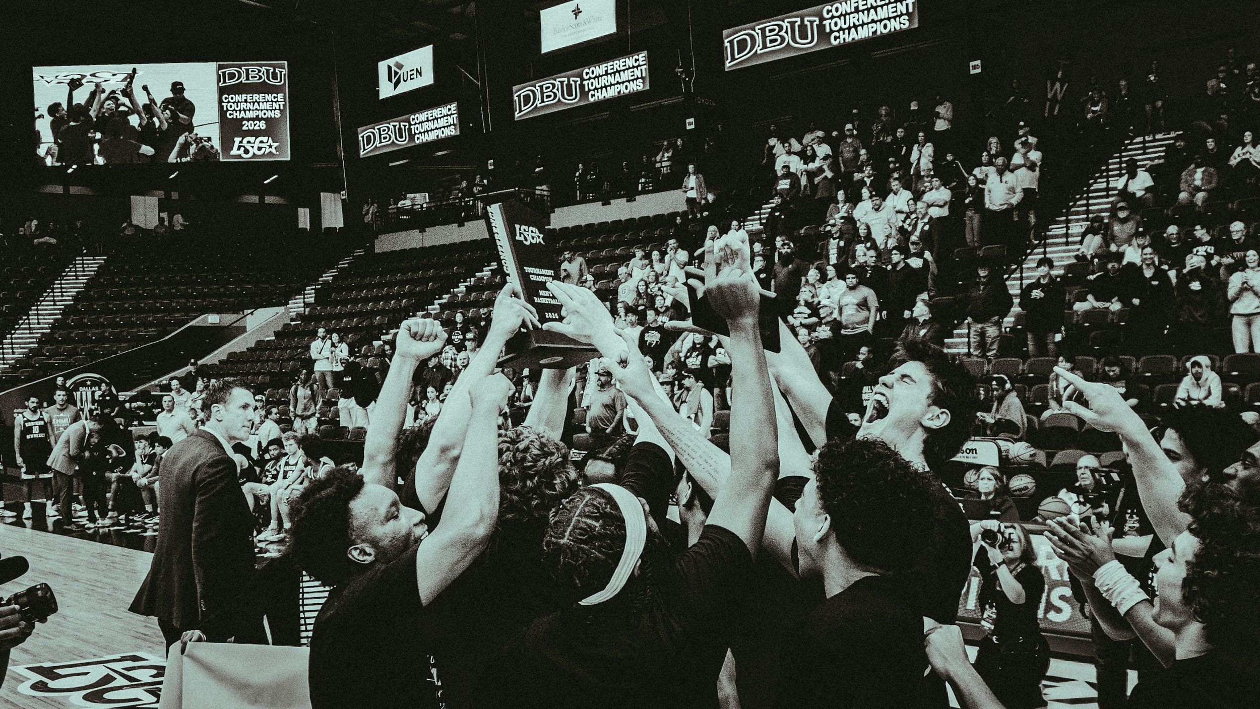Celebration at a basketball tournament victory, with players and fans cheering and holding up a trophy inside an arena with digital screens displaying 'DBU Conference Tournament Champions 2026'.