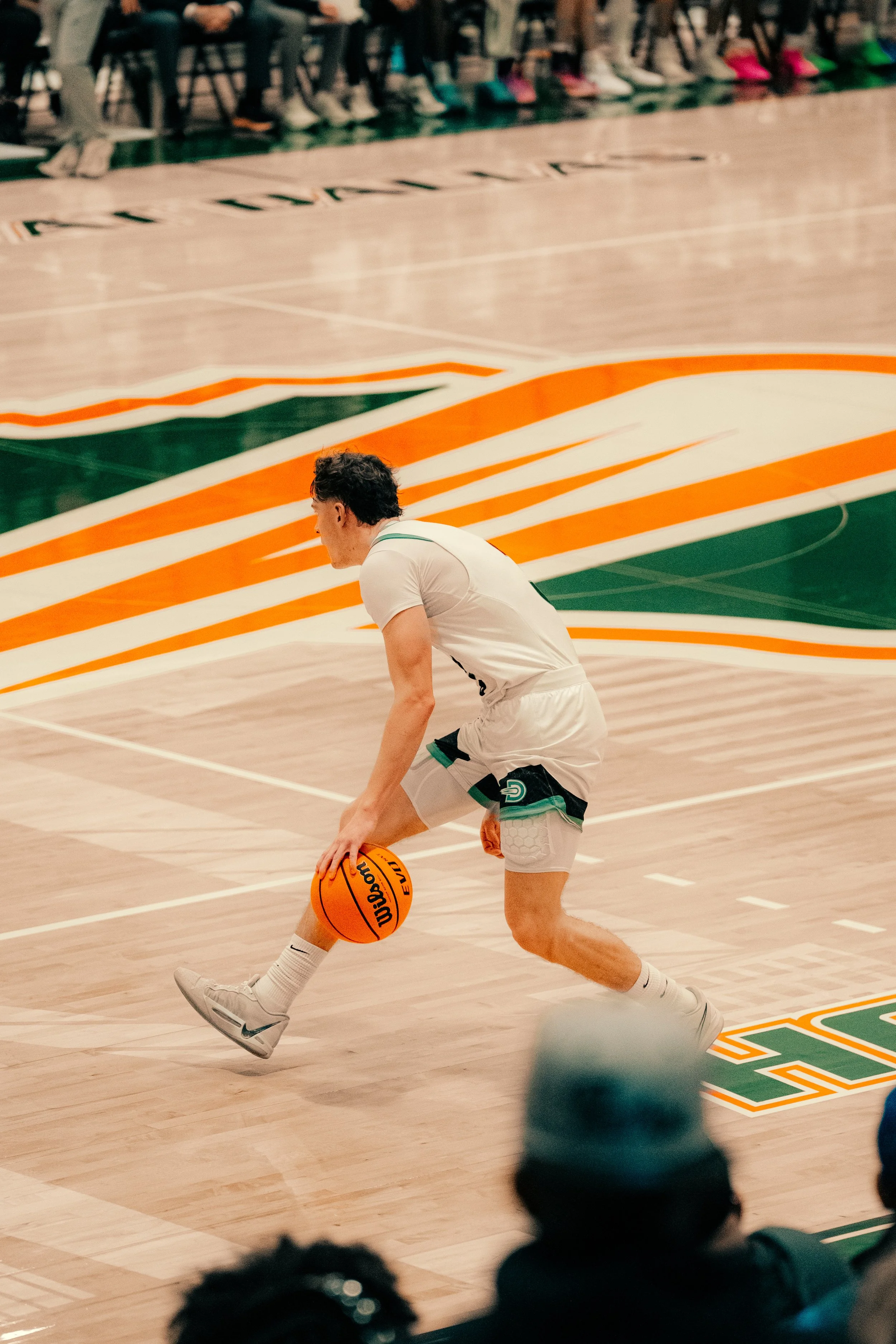 A basketball player in a white uniform dribbling a basketball on a basketball court during a game or practice