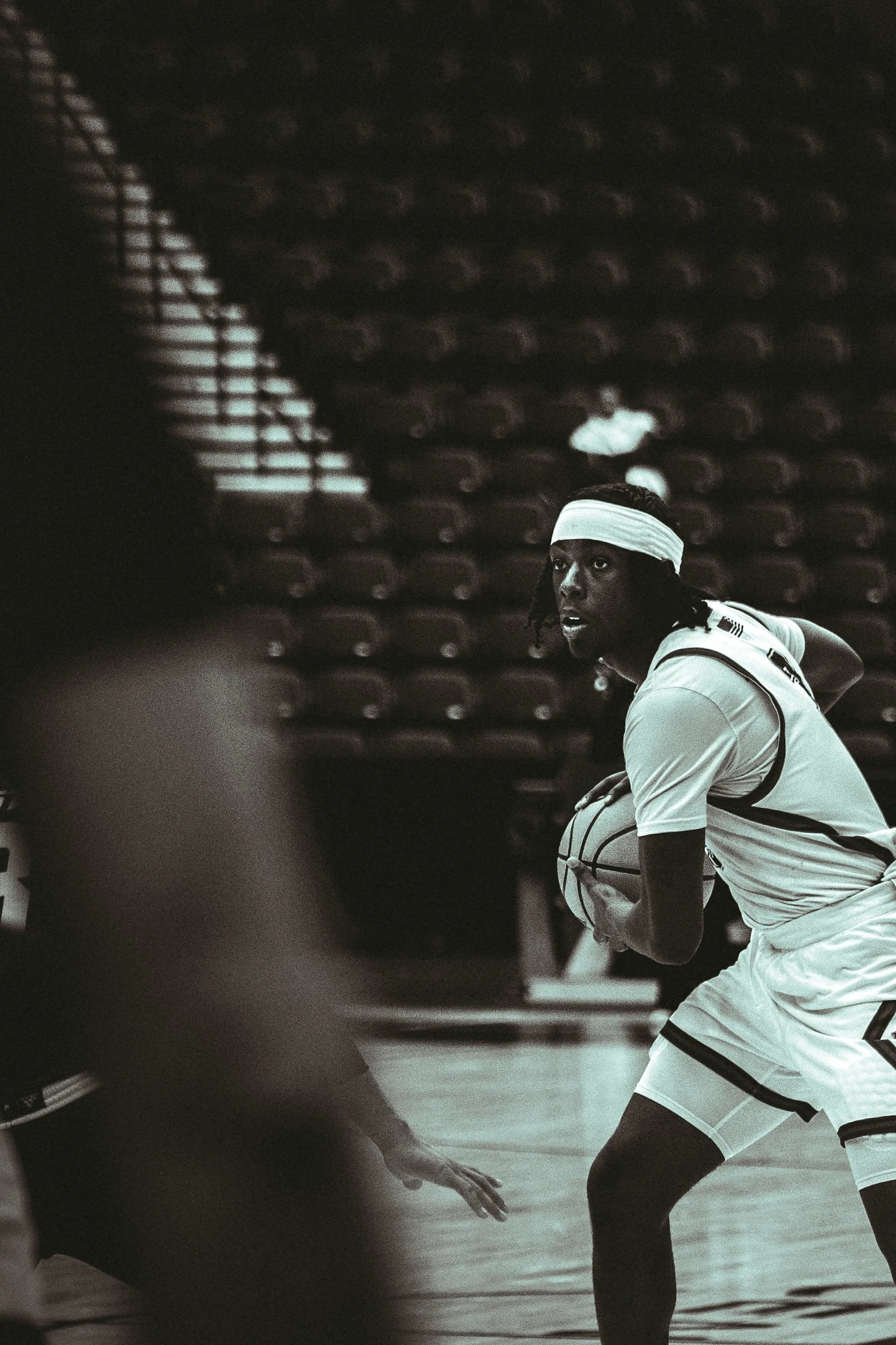 A female basketball player in a white uniform and headband is dribbling a basketball on the court during a game.