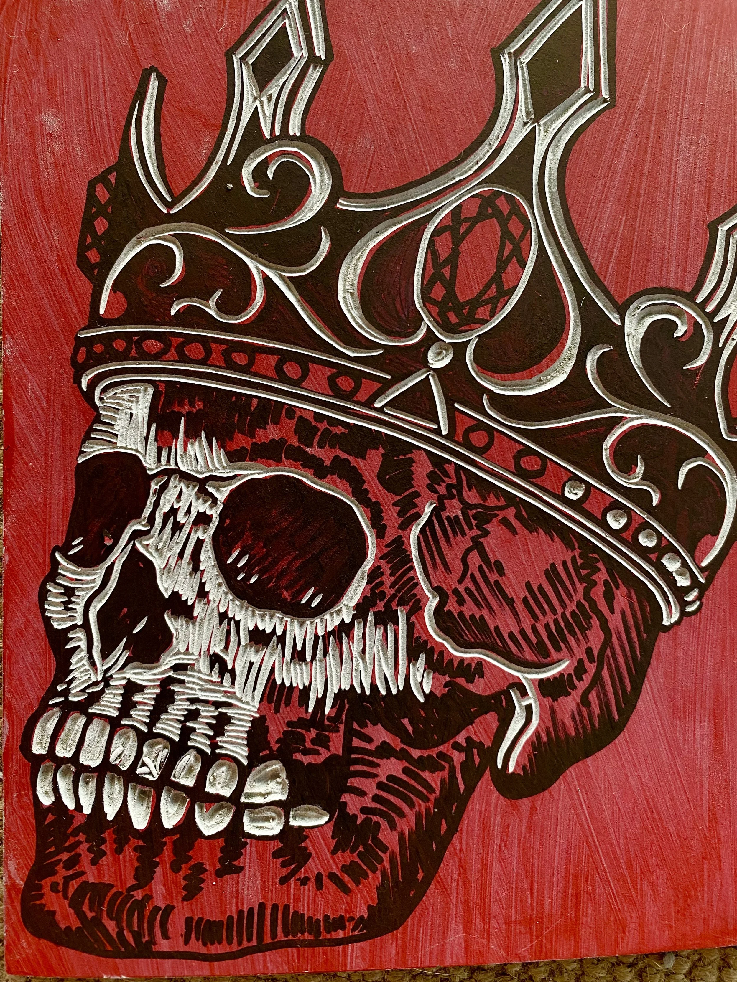 A close-up of a red painted wall with a large black and white graffiti sketch of a skull wearing a crown.