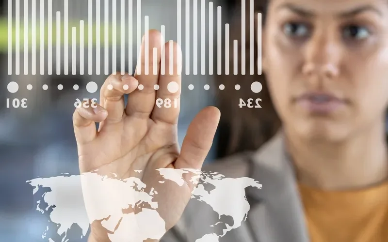 A woman interacting with a transparent digital interface showing a world map and bar graphs.
