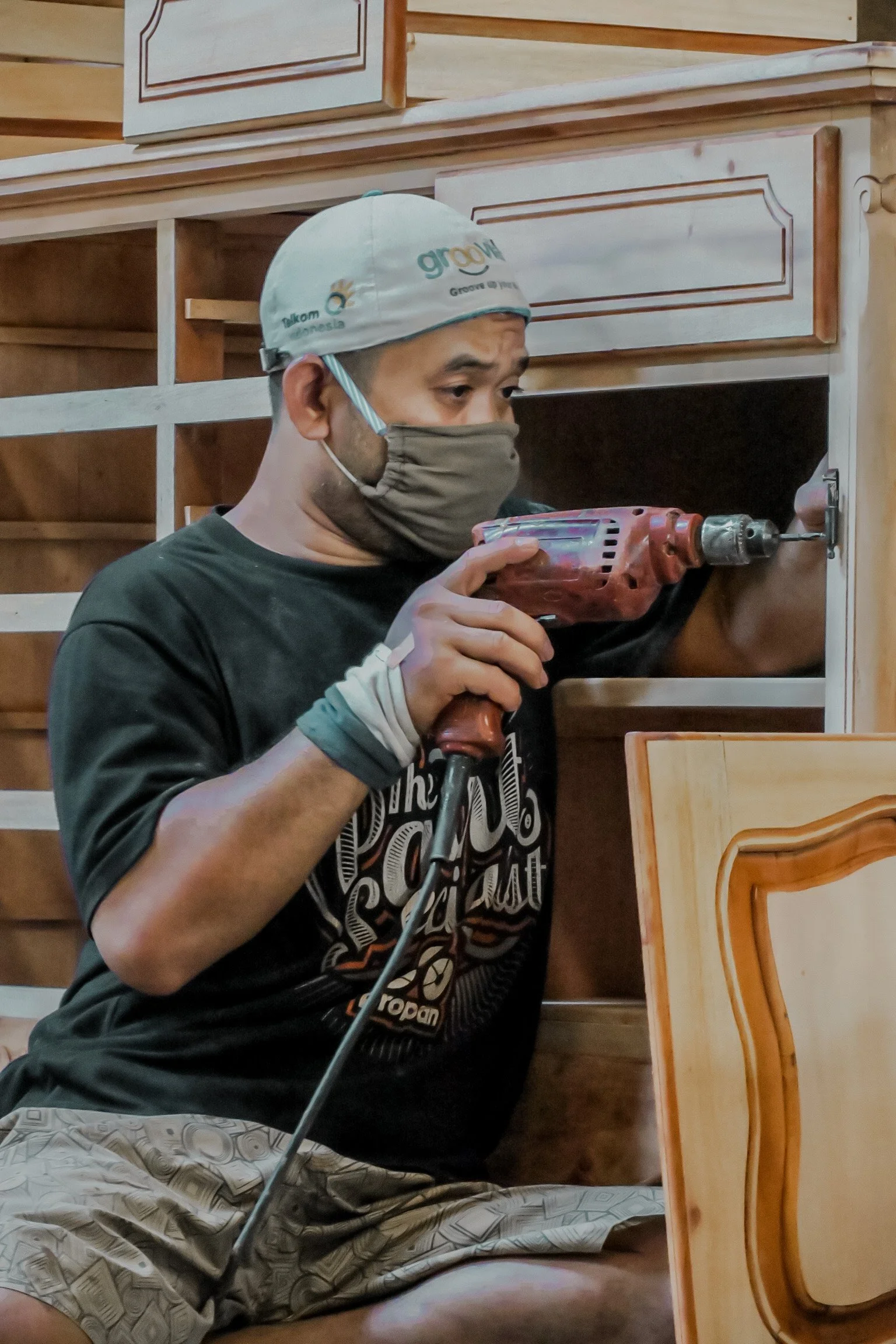 Man using a cordless drill to install or fix a teak wood cabinet or drawer. Teak Furniture Jepara, wholesale Indonesian teak furniture, custom outdoor teak furniture manufacturer, Jepara teak furniture supplier. 