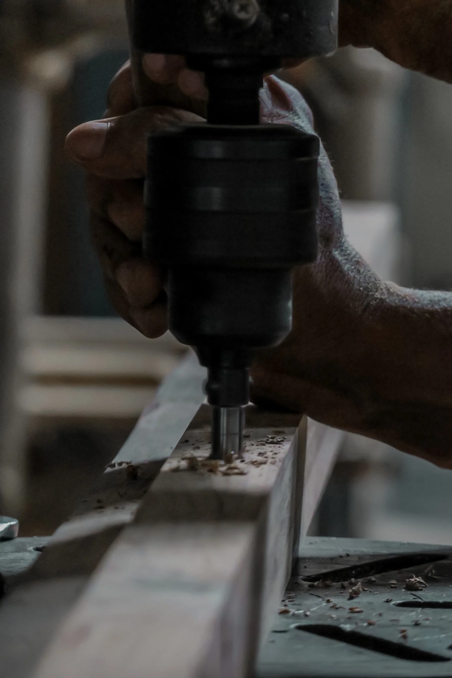 Close-up of a person's hand holding a router drill while working on a wooden piece, with wood shavings scattered on the surface. Teak Furniture Jepara, wholesale Indonesian teak furniture, custom outdoor teak furniture manufacturer, Jepara teak furni