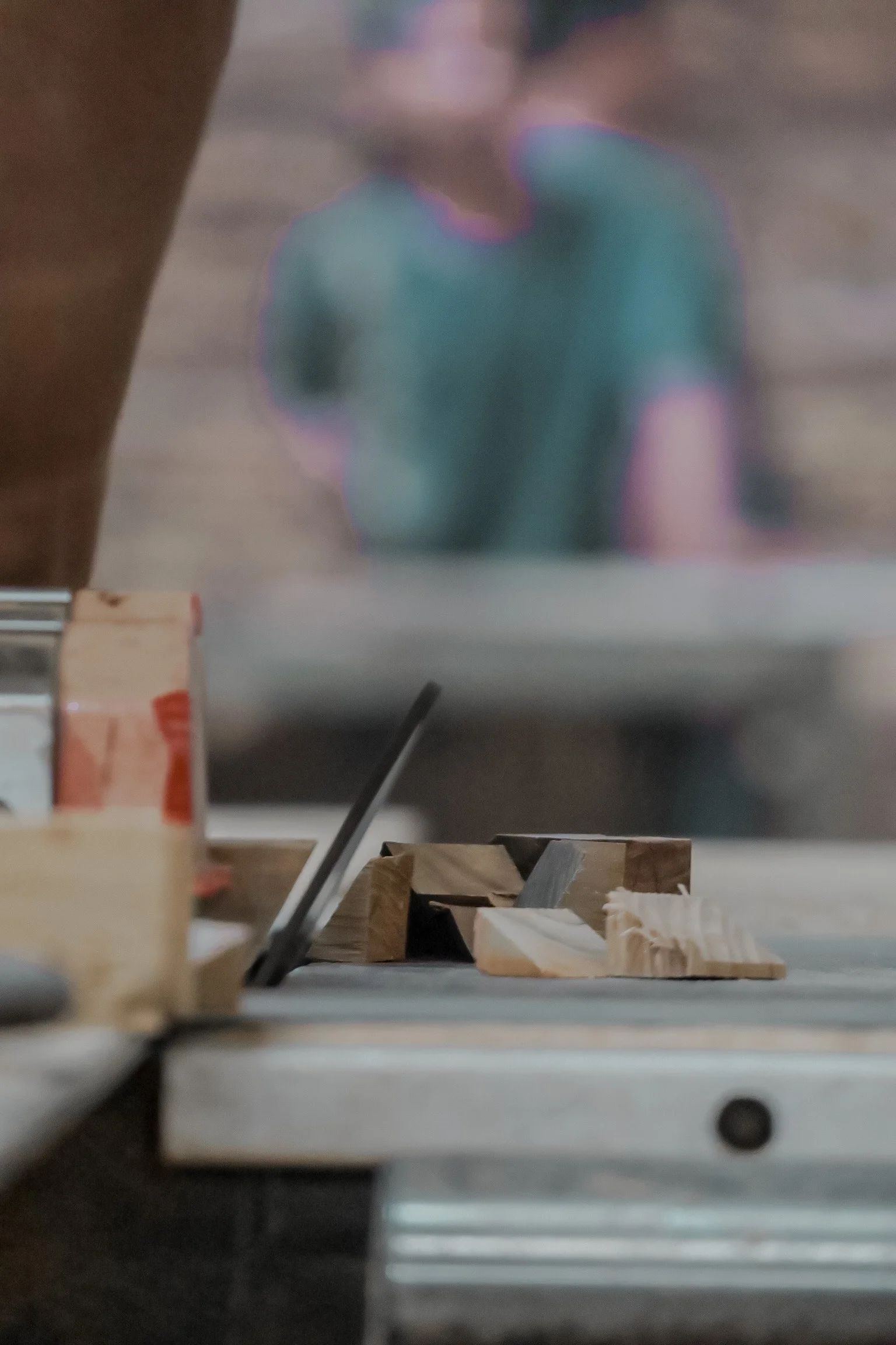 A blurry photograph of a workspace with scattered wood pieces and tools, viewed from beneath a table or workbench.