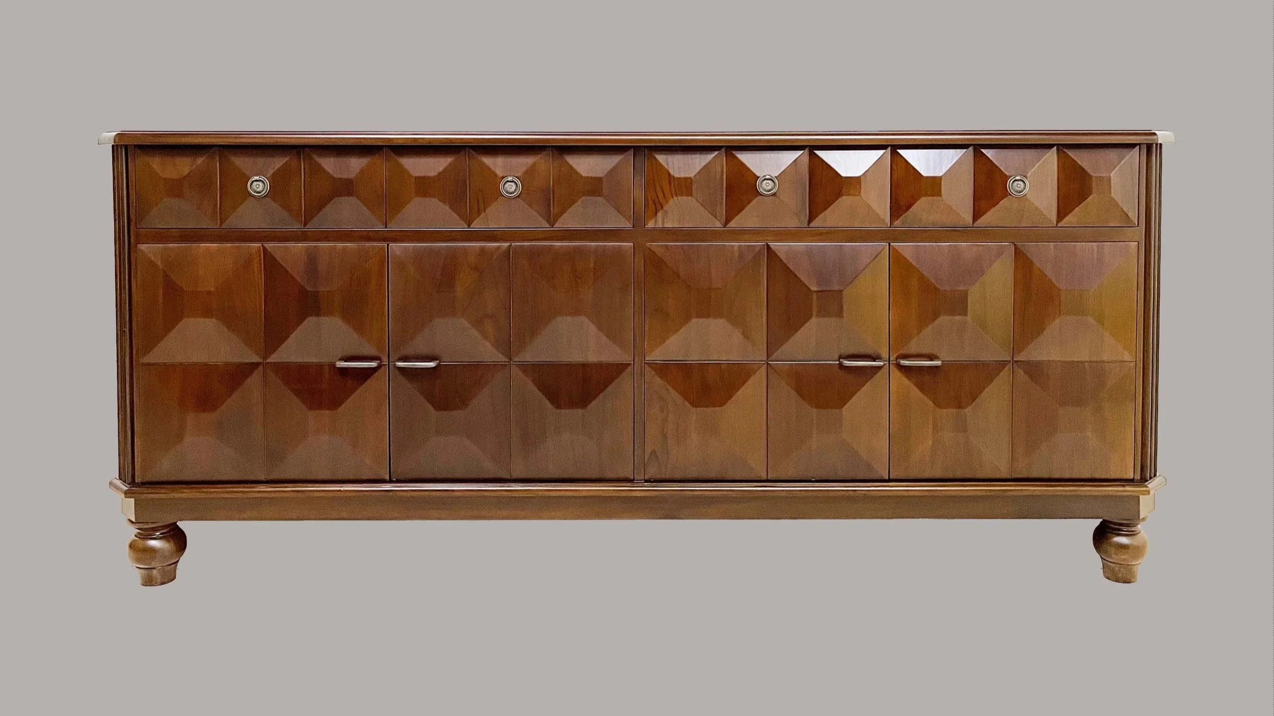 A mid-century modern wooden sideboard with geometric beveled panels and metal handles, supported by rounded turned legs, set against a gray background.