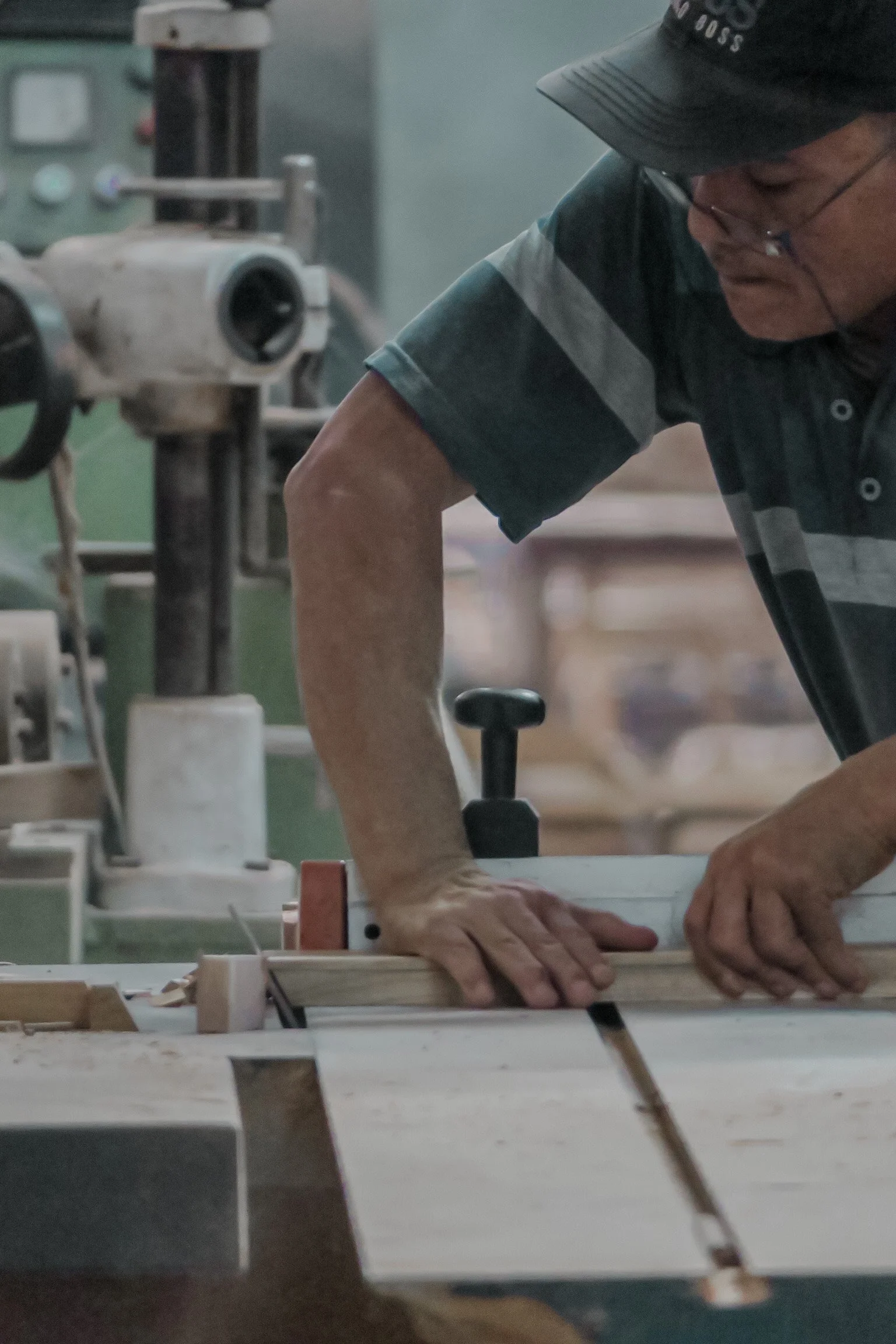 A man in a woodworking shop, using a saw on a piece of teak wood. He is wearing safety glasses with his hands firmly holding the wood in place. Teak Furniture Jepara, wholesale Indonesian teak furniture, custom outdoor teak furniture manufacturer