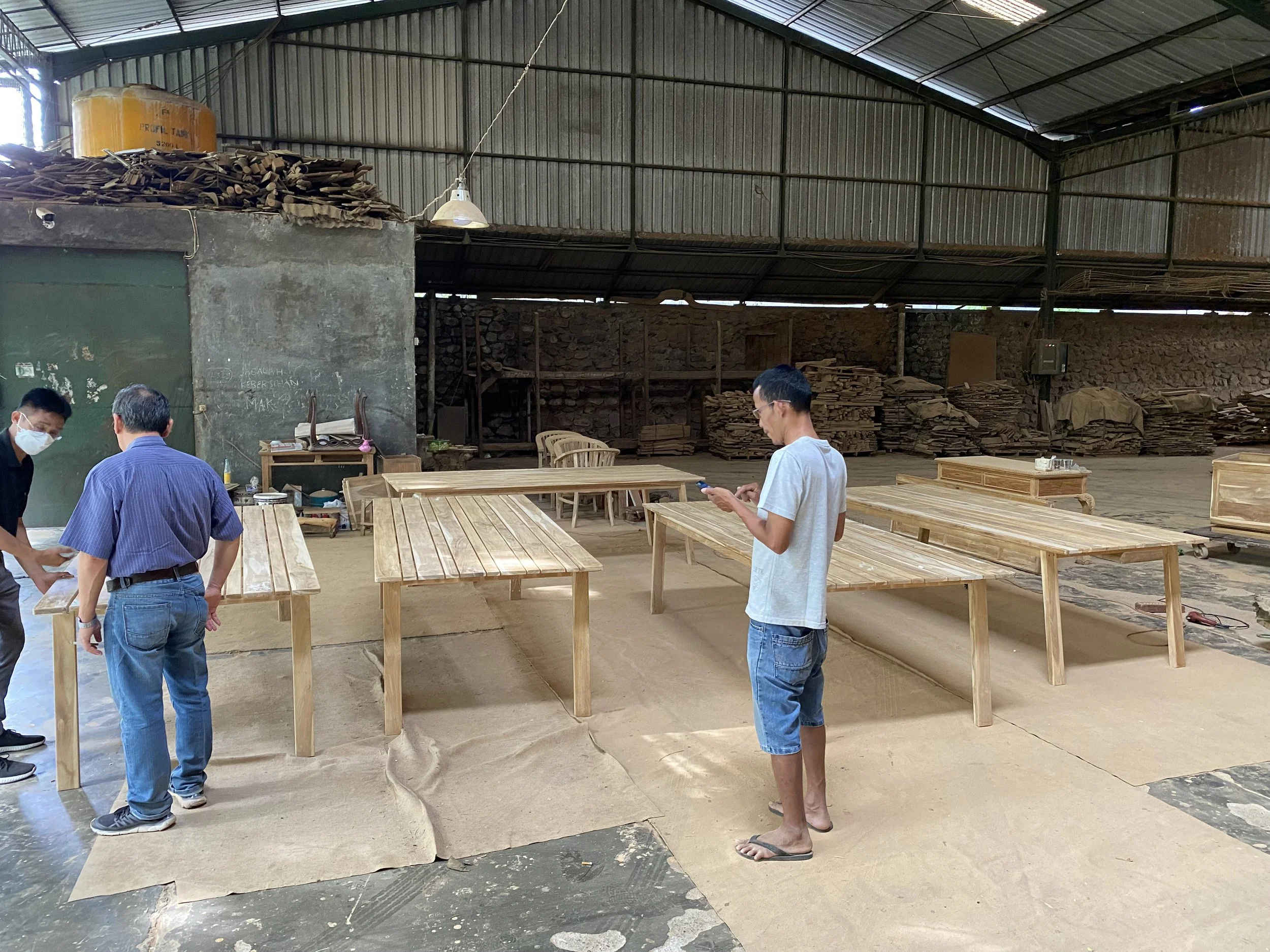 Three men are standing around teak wooden tables. Teak Furniture Jepara, wholesale Indonesian teak furniture, custom outdoor teak furniture manufacturer, Jepara teak furniture supplier. 