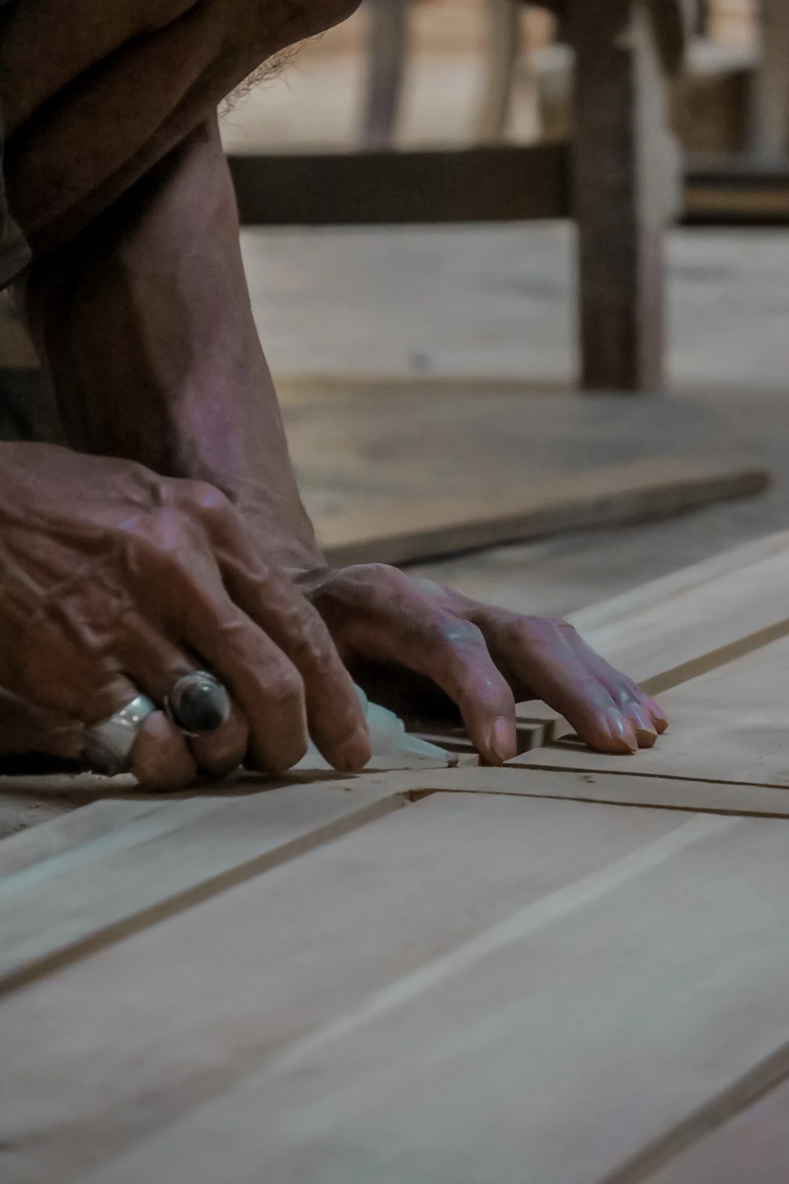 A close-up of a person's hands and forearms resting on a wooden surface, with wooden furniture in the background. Teak Furniture Jepara, wholesale Indonesian teak furniture, custom outdoor teak furniture manufacturer, Jepara teak furniture supplier. 