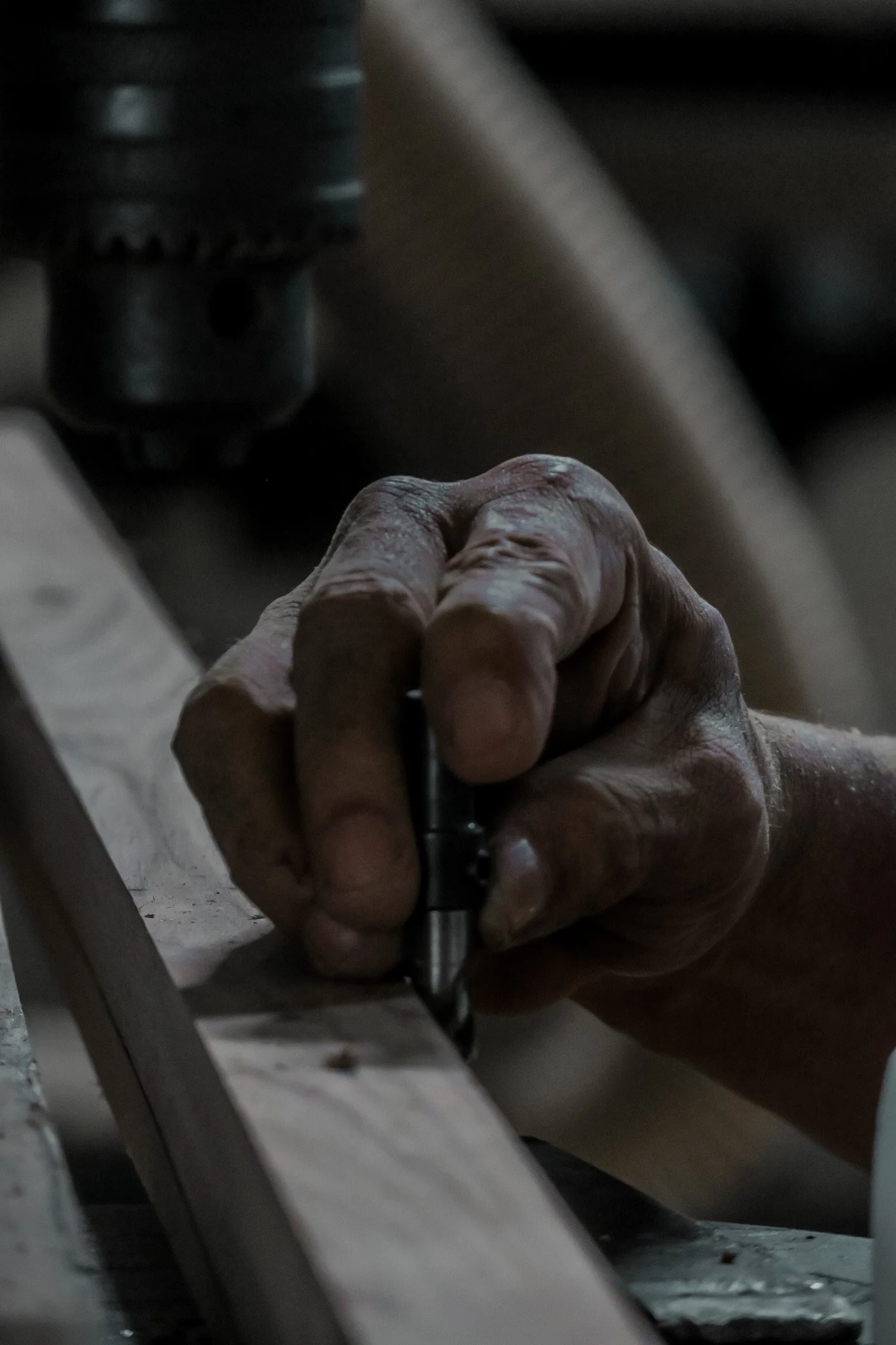 Close-up of an elderly person's hand holding a writing instrument, writing on a piece of paper, with machinery or tools in the background. Teak Furniture Jepara, wholesale Indonesian teak furniture, custom outdoor teak furniture manufacturer, Jepara 