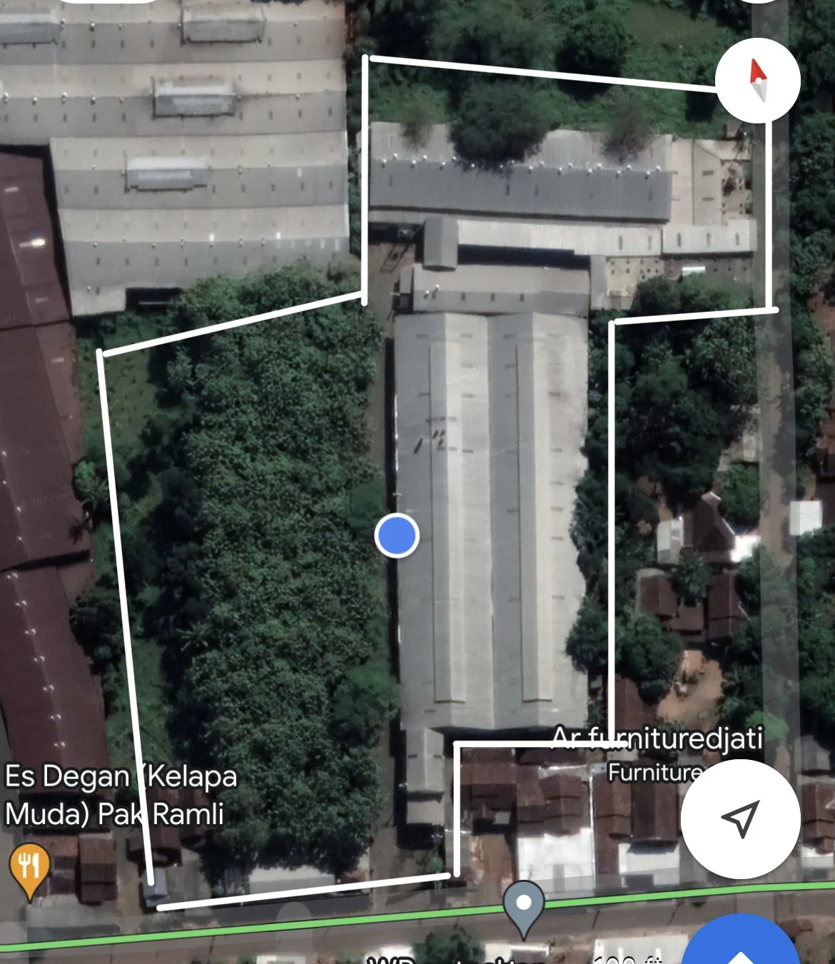 An aerial view of a property with buildings, trees, and surrounding residential area, marked with outlined boundaries and directional lines on a map.