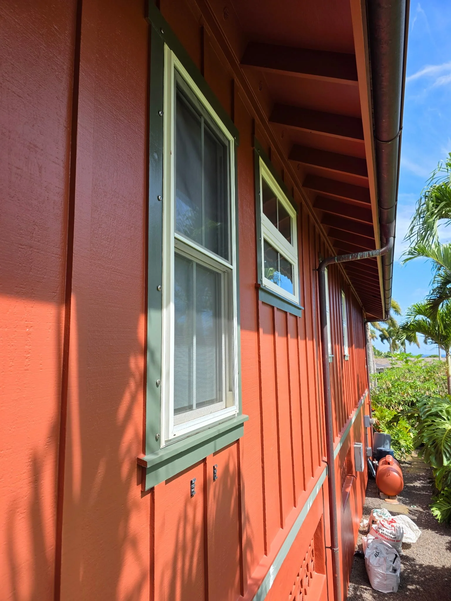 Close-up view of the side of a red house with five white-framed windows and green trim in Poipu, Kauai, Hawaii with full exterior repaint