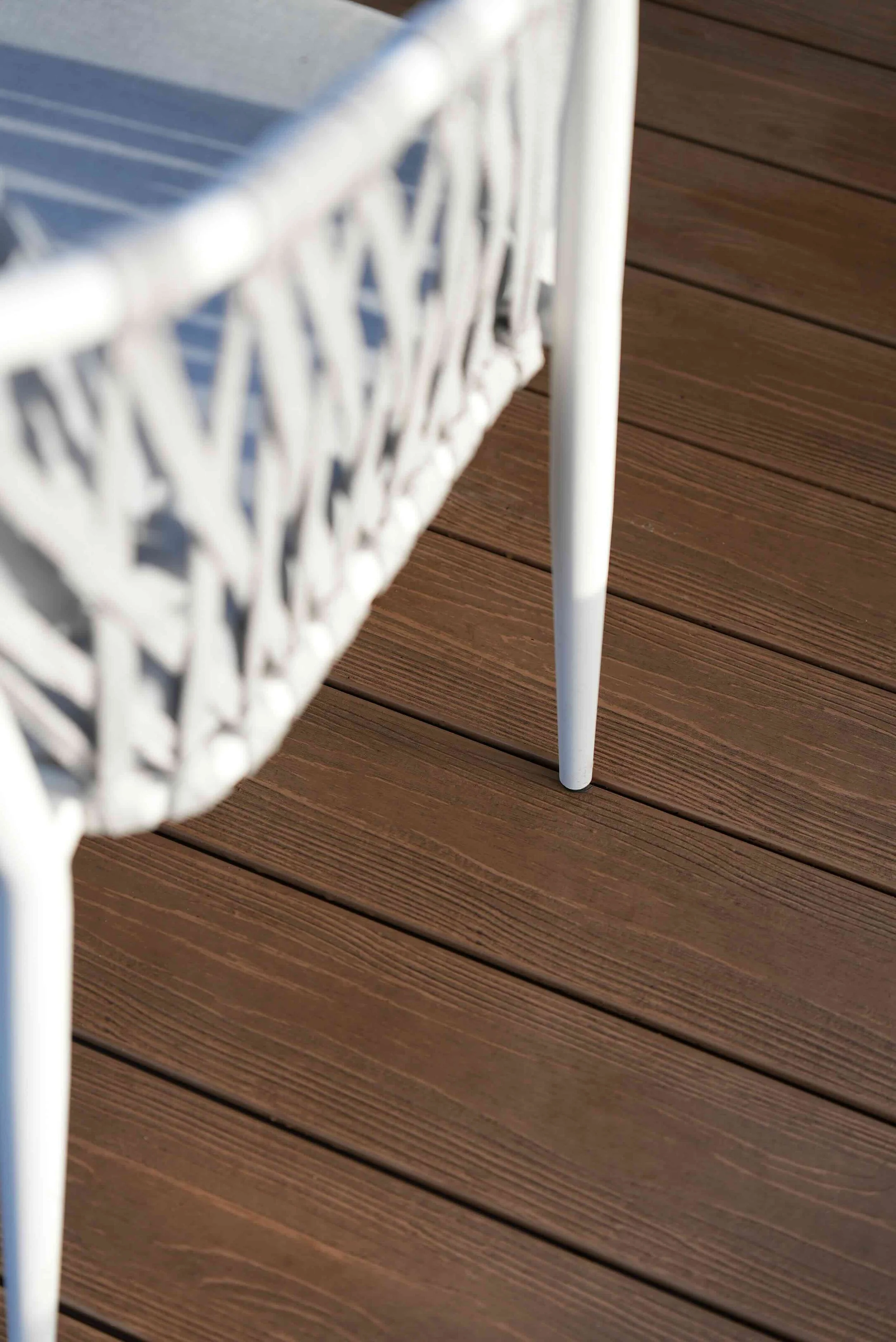 Close-up of a white metal outdoor chair with a decorative backrest placed on brown wooden decking.