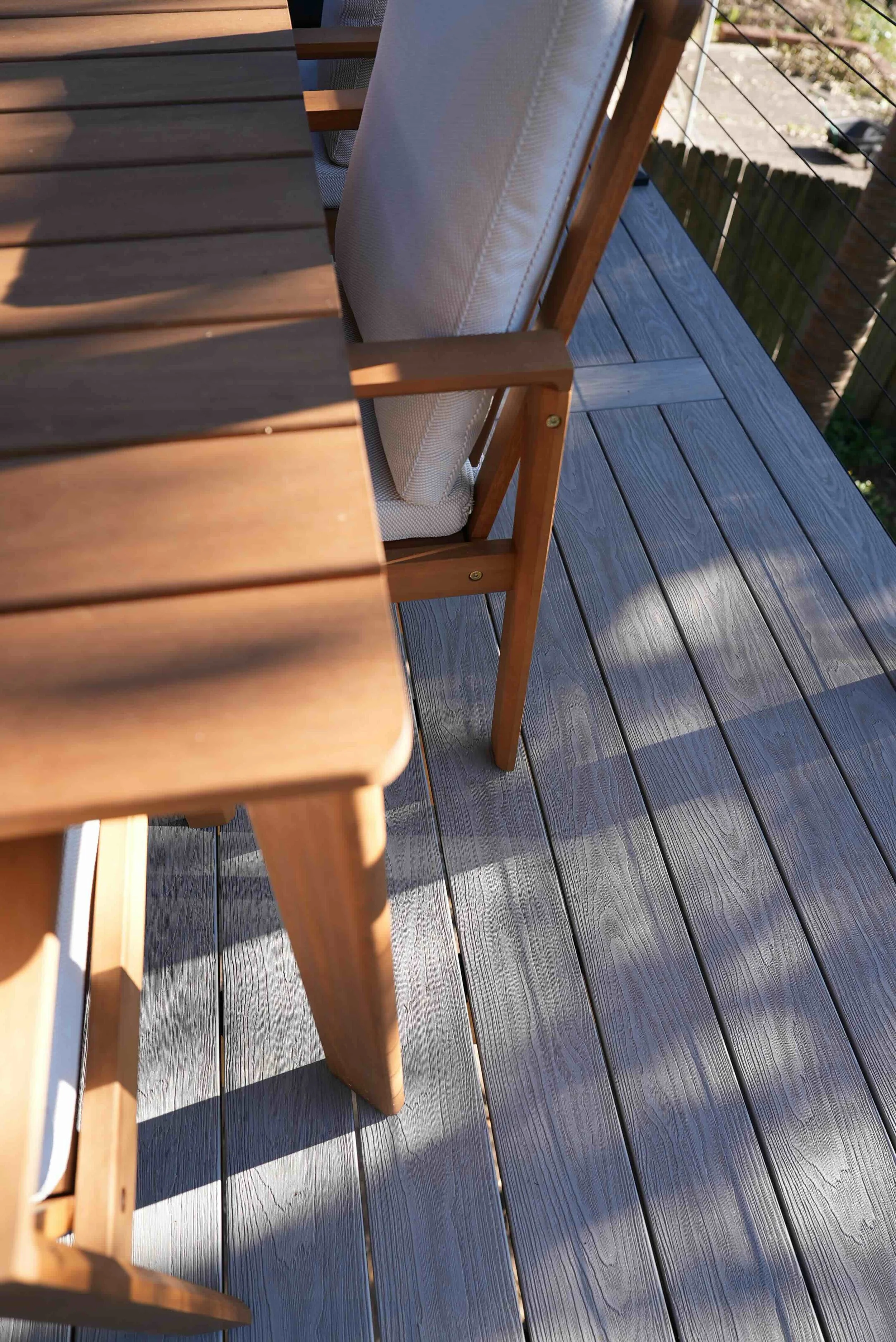 Close-up of outdoor wooden patio furniture and flooring with sunlight and shadows.