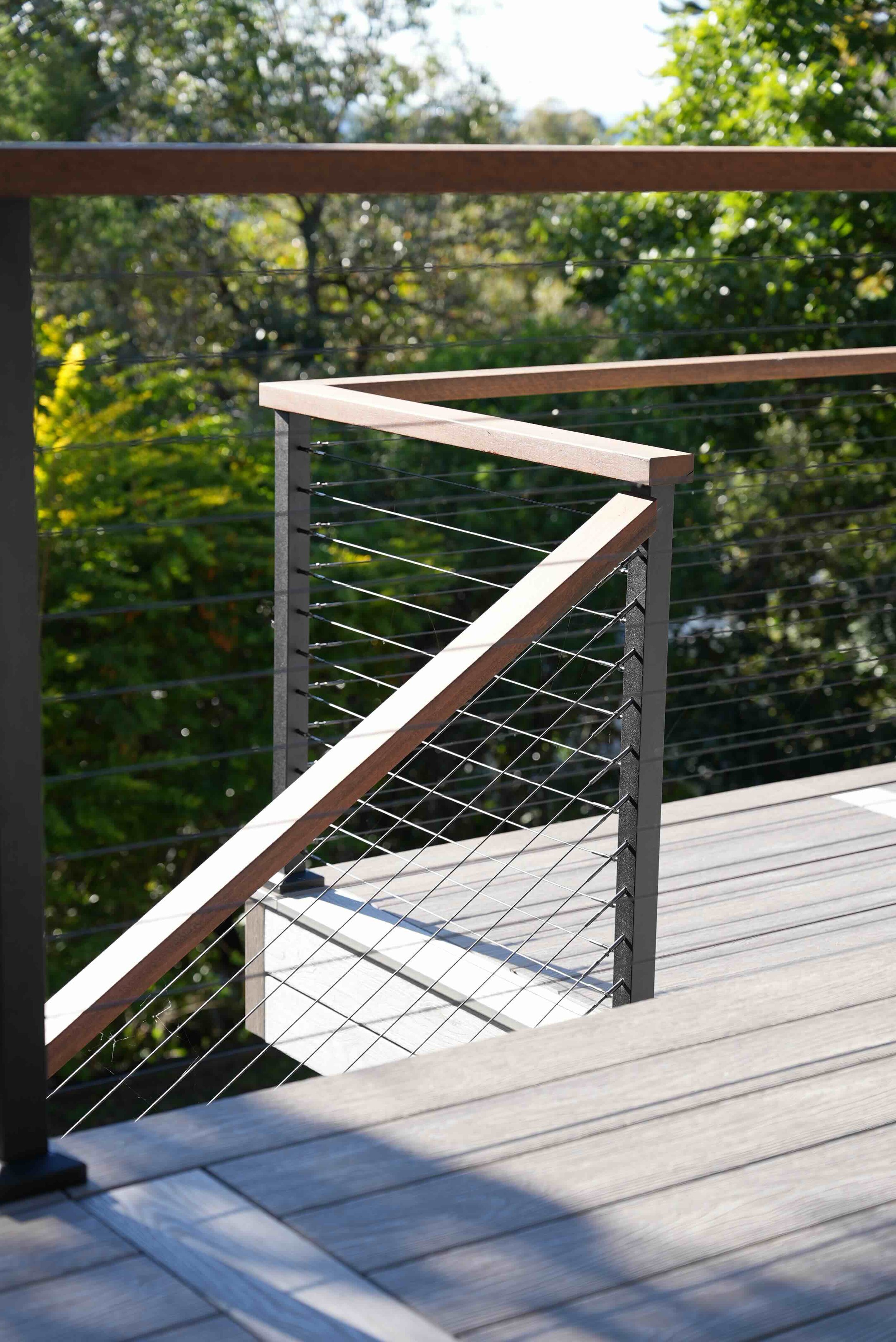 Outdoor deck with modern metal and wood railing, overlooking lush green trees and blue sky with some clouds.