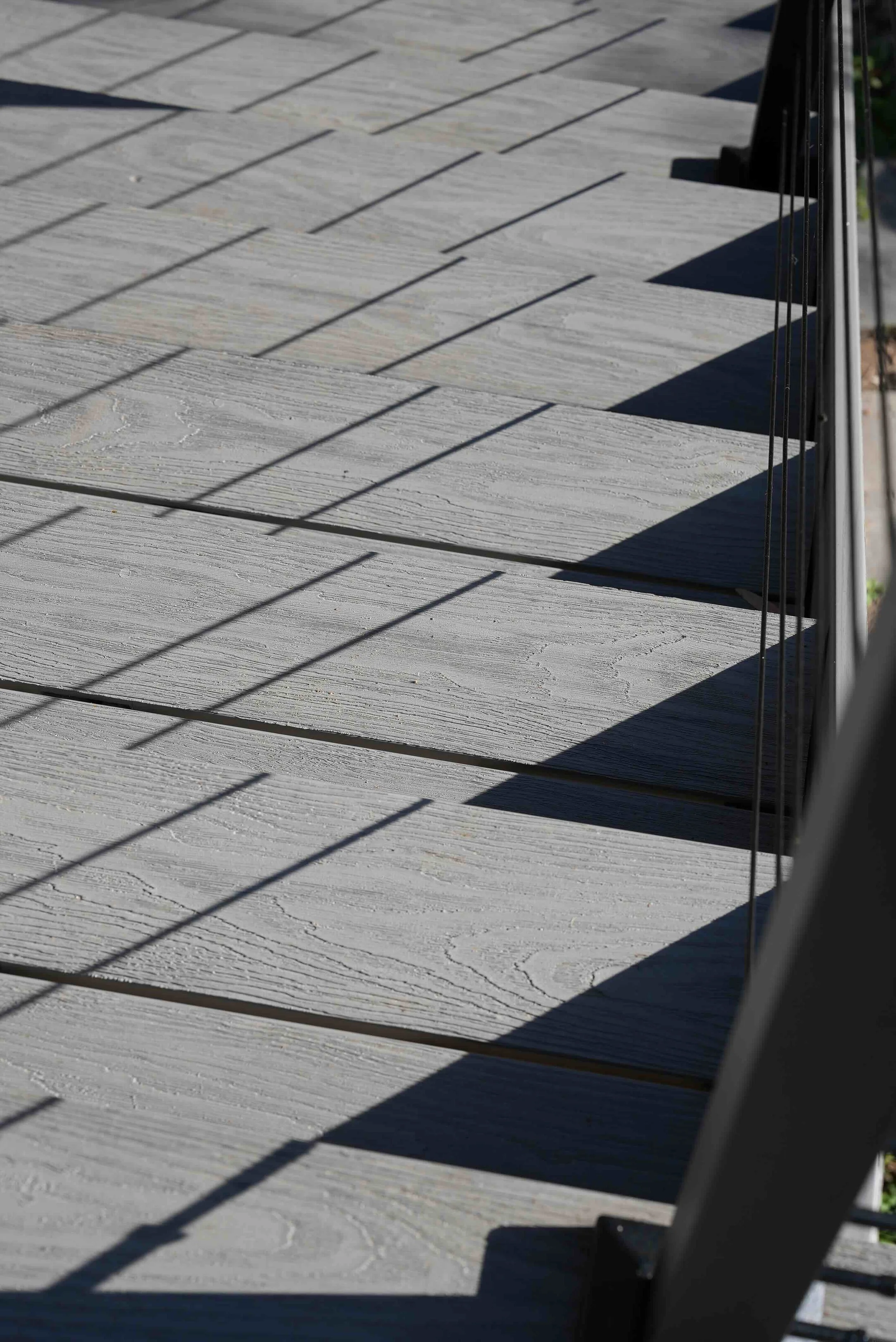 Close-up of a wooden deck with sunlight casting shadows of a metal railing