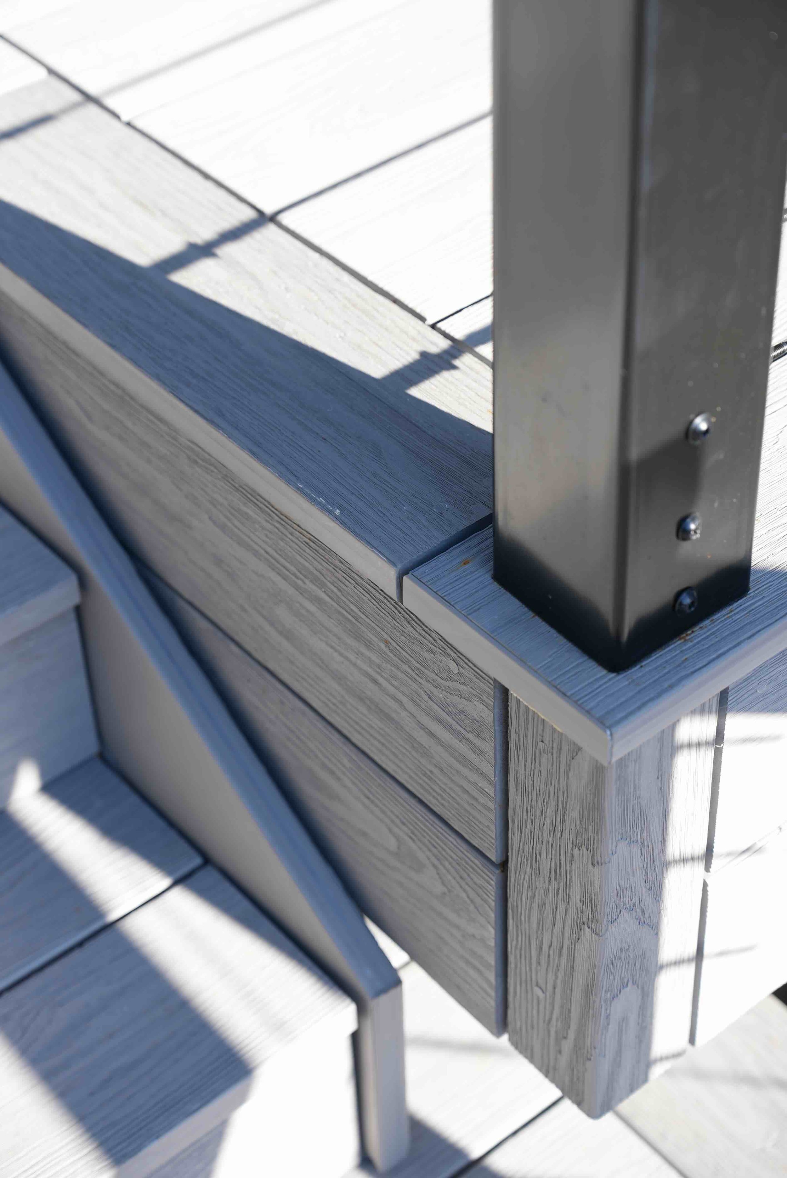 Close-up of a section of outdoor wooden bench with metal support, showing whitewashed wooden slats and shadows.