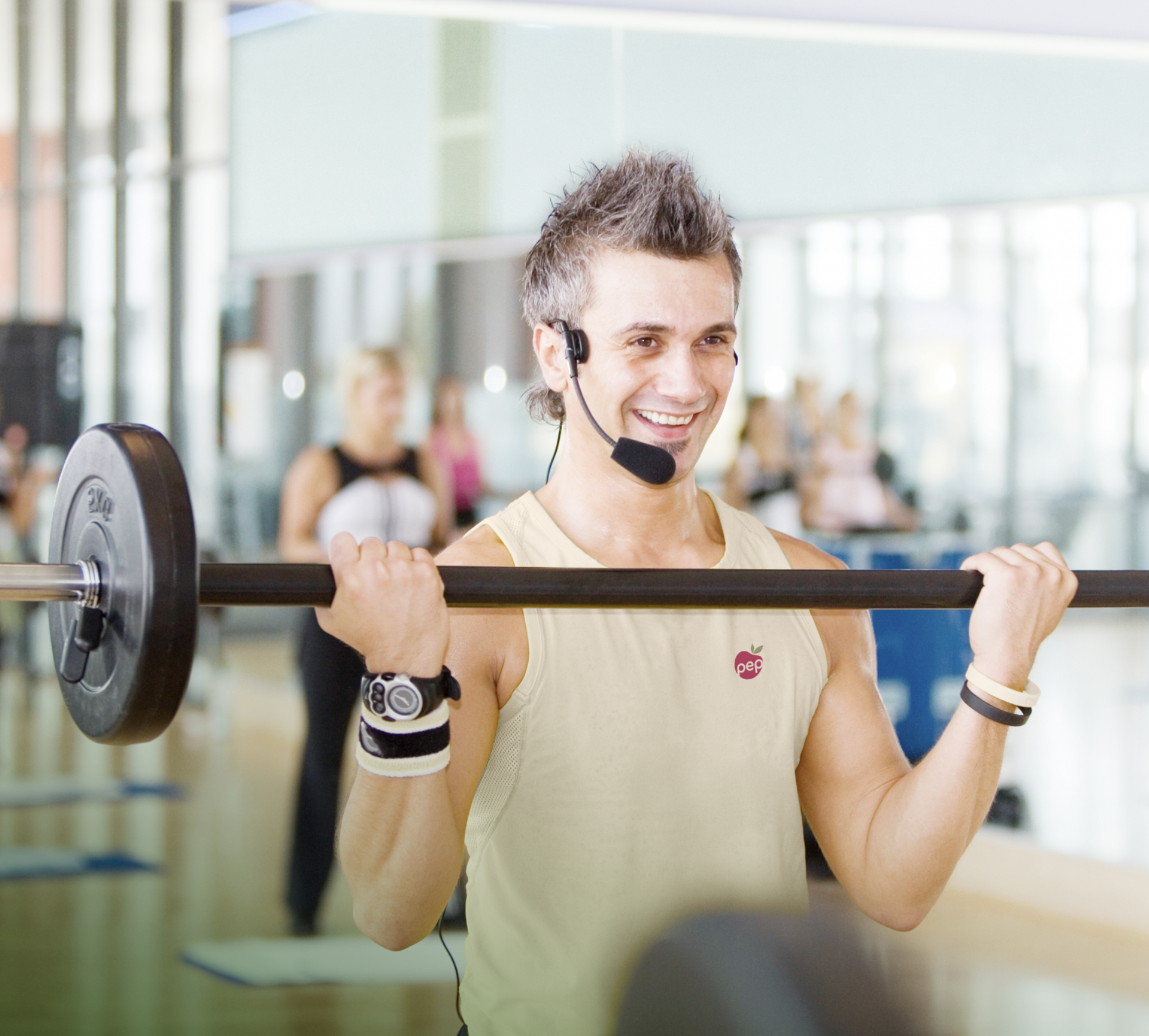 Fitness-Trainer beim Gewichtheben in einem Fitnessstudio, trägt einen Trainingshandschuh und ein Headset, lächelt, Hintergrund mit anderen Trainierenden.