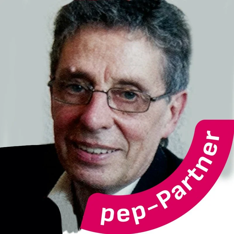 Ein Mann mit Brille, grauem Haar und Anzug, lächelnd, mit pinkfarbiger Banderole mit weißer Schrift 'pep-Partner'