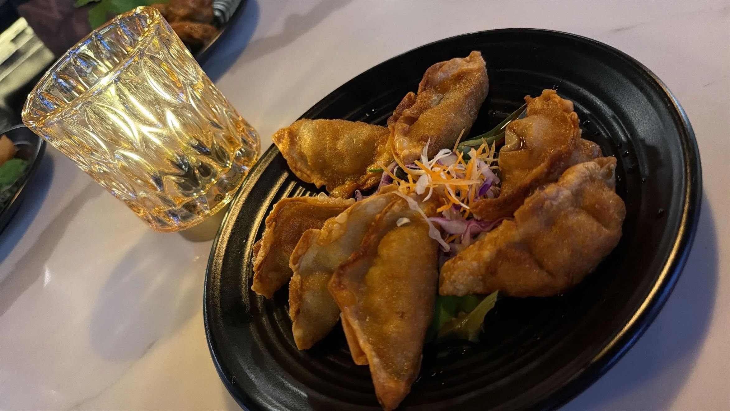 Plate of fried dumplings with shredded vegetables and a glass of yellow-colored beverage.