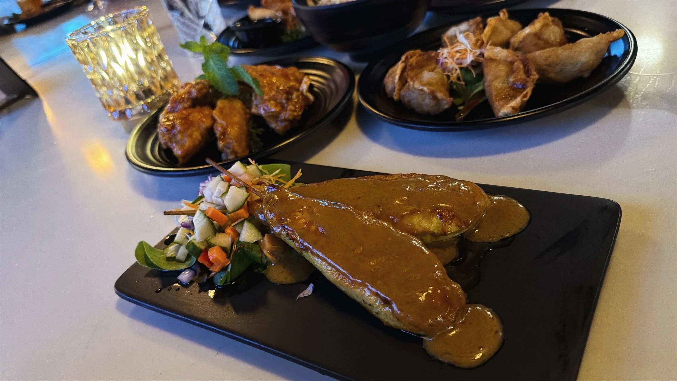 Three black plates with Asian dishes, including a grilled fish fillet with brown sauce, chicken wings with sauce and garnish, and fried shrimp with garnishes and vegetables.