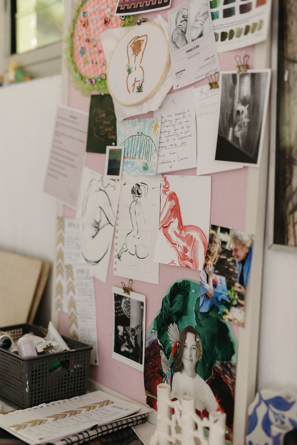 Pink bulletin board covered with artwork, photographs, handwritten notes, embroidery, and collage pieces.