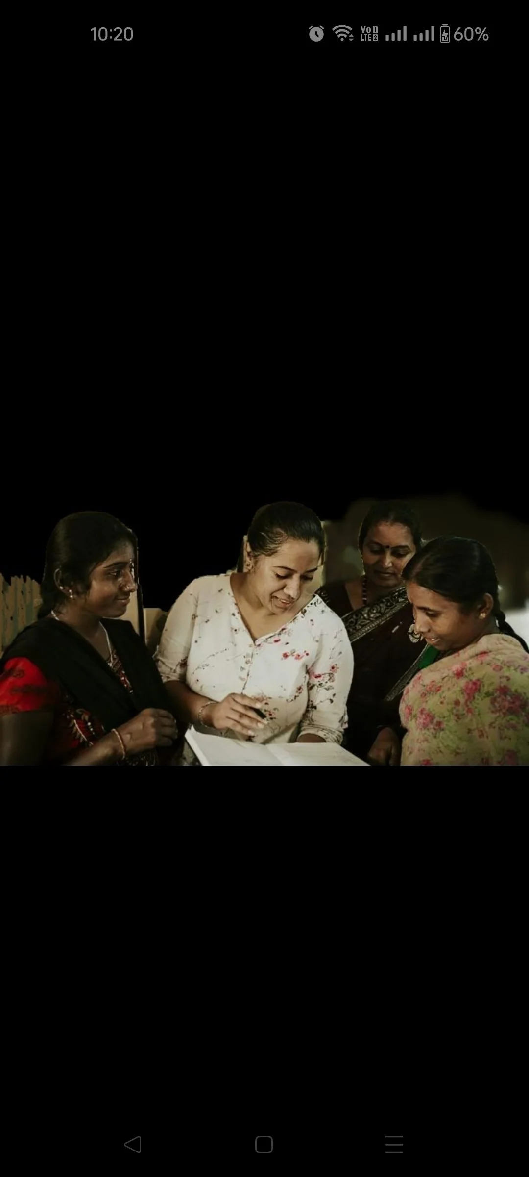 Four women gathered around a book, reading and discussing together outdoors at night.