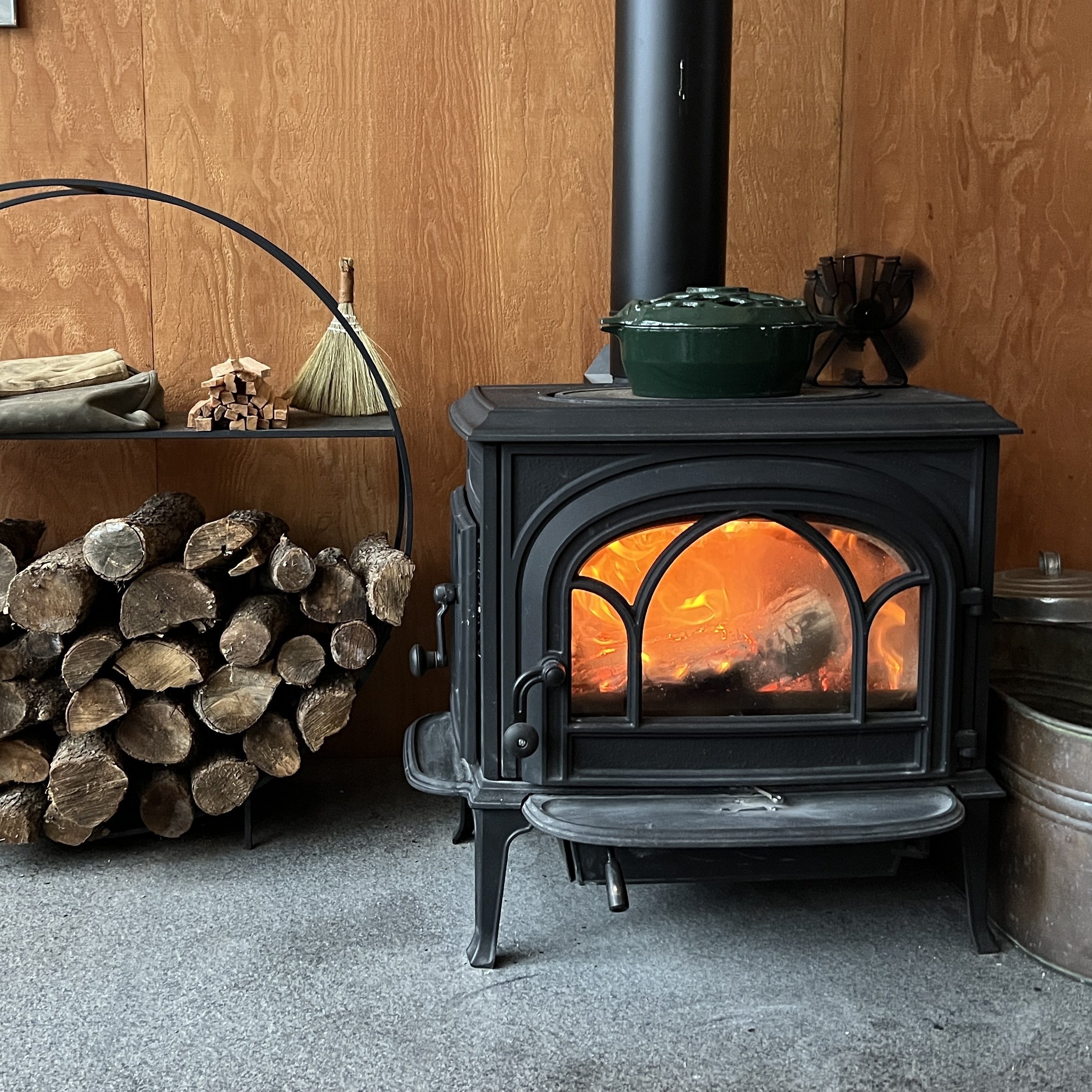 a lit woodstove next to stacked firewood