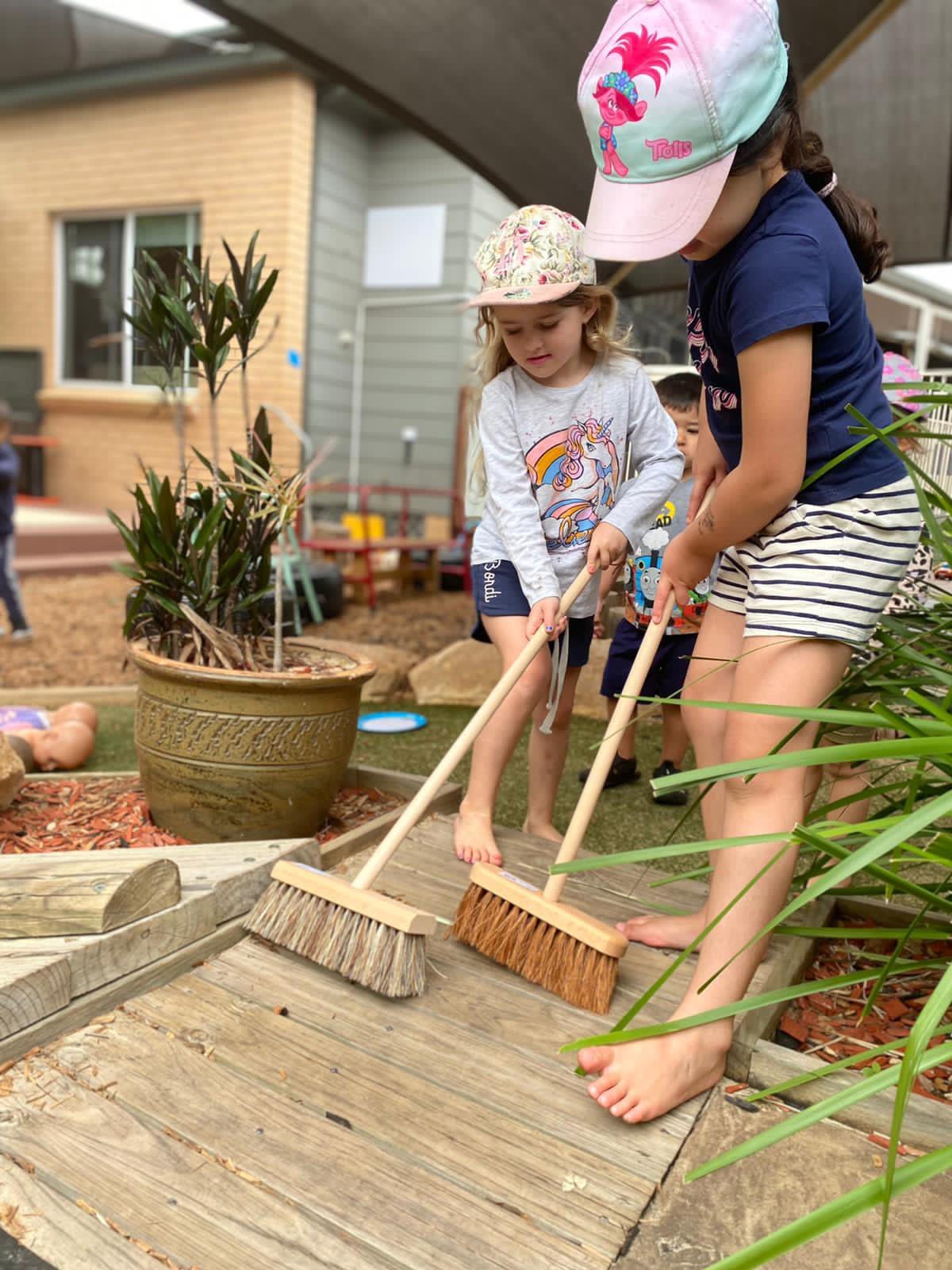 Children sweeping wooden deck in a backyard garden.