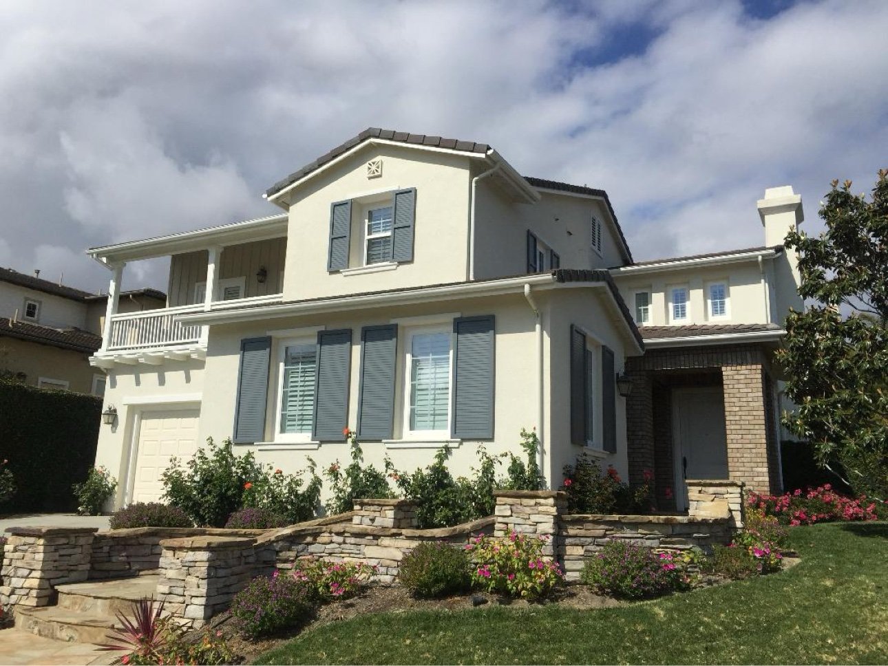 Exterior repaint of two-story home — cream stucco with blue-gray shutters and stone accents