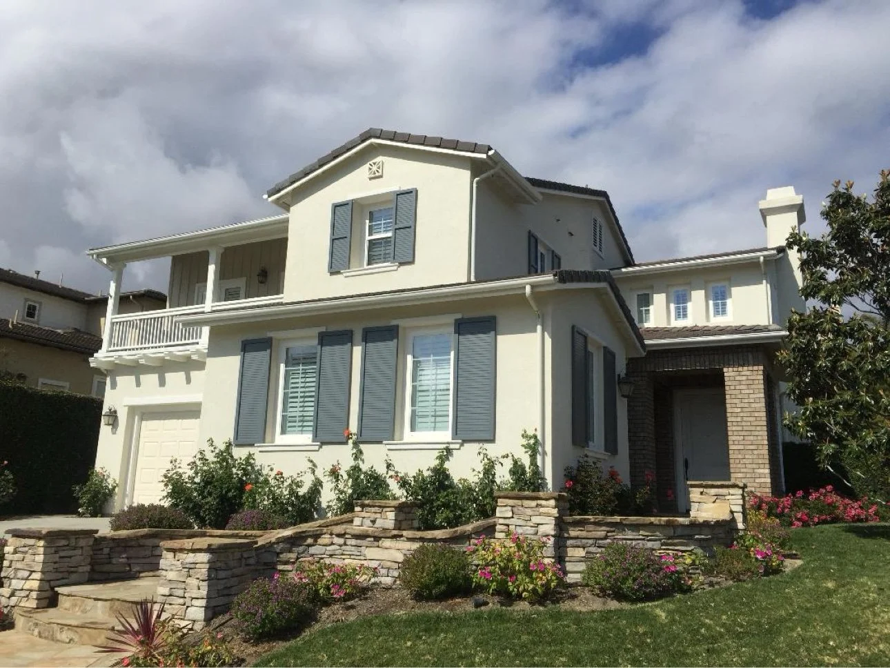 Two-story home exterior — beige stucco with blue-gray shutters, tile roof, and stone veneer accents